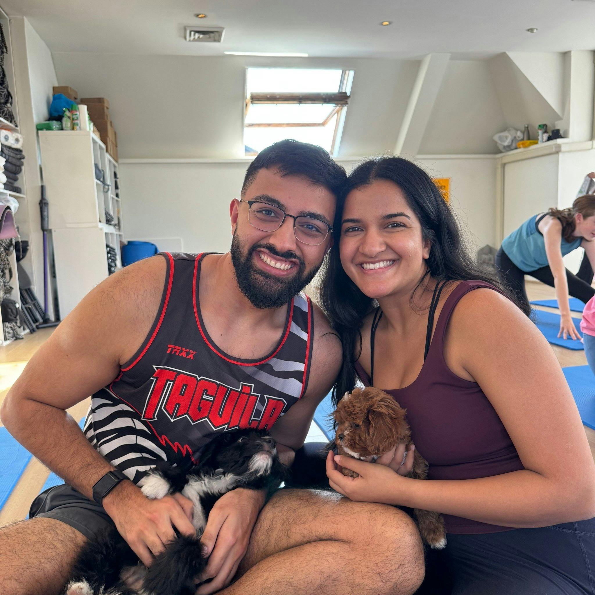 A woman and young girl sitting on blue mats smiling with a small black and white puppy at Doga Sydne