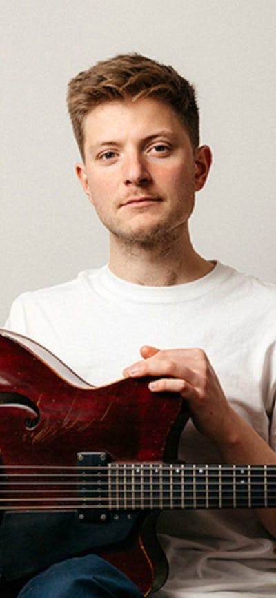 Photo of a man sitting holding a jazz guitar