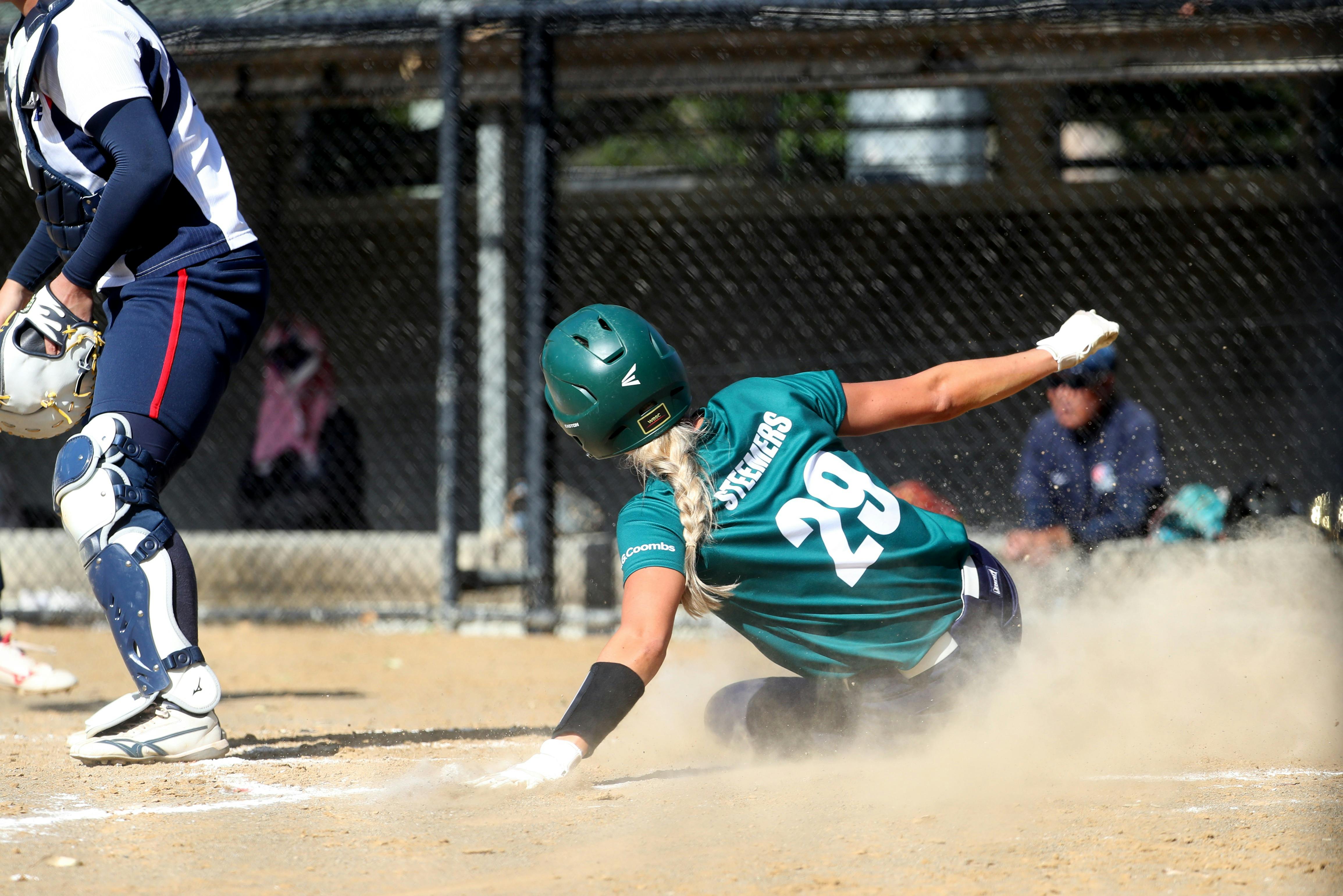 Softball player slides into home plate through dust as catcher waits during competitive match.  Prov