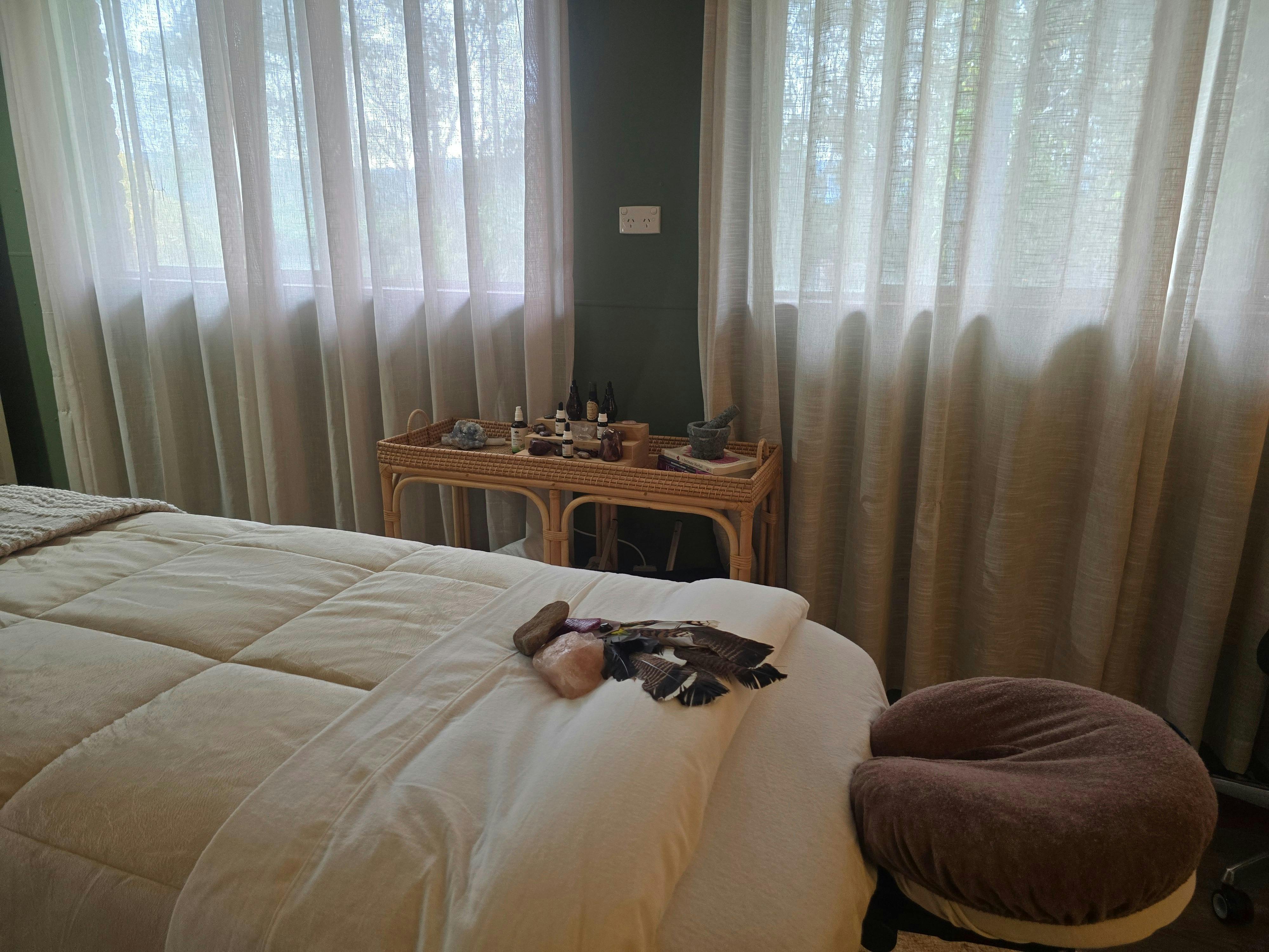 Massage table with soft cream bedding beside a trolley holding herbal remedies.