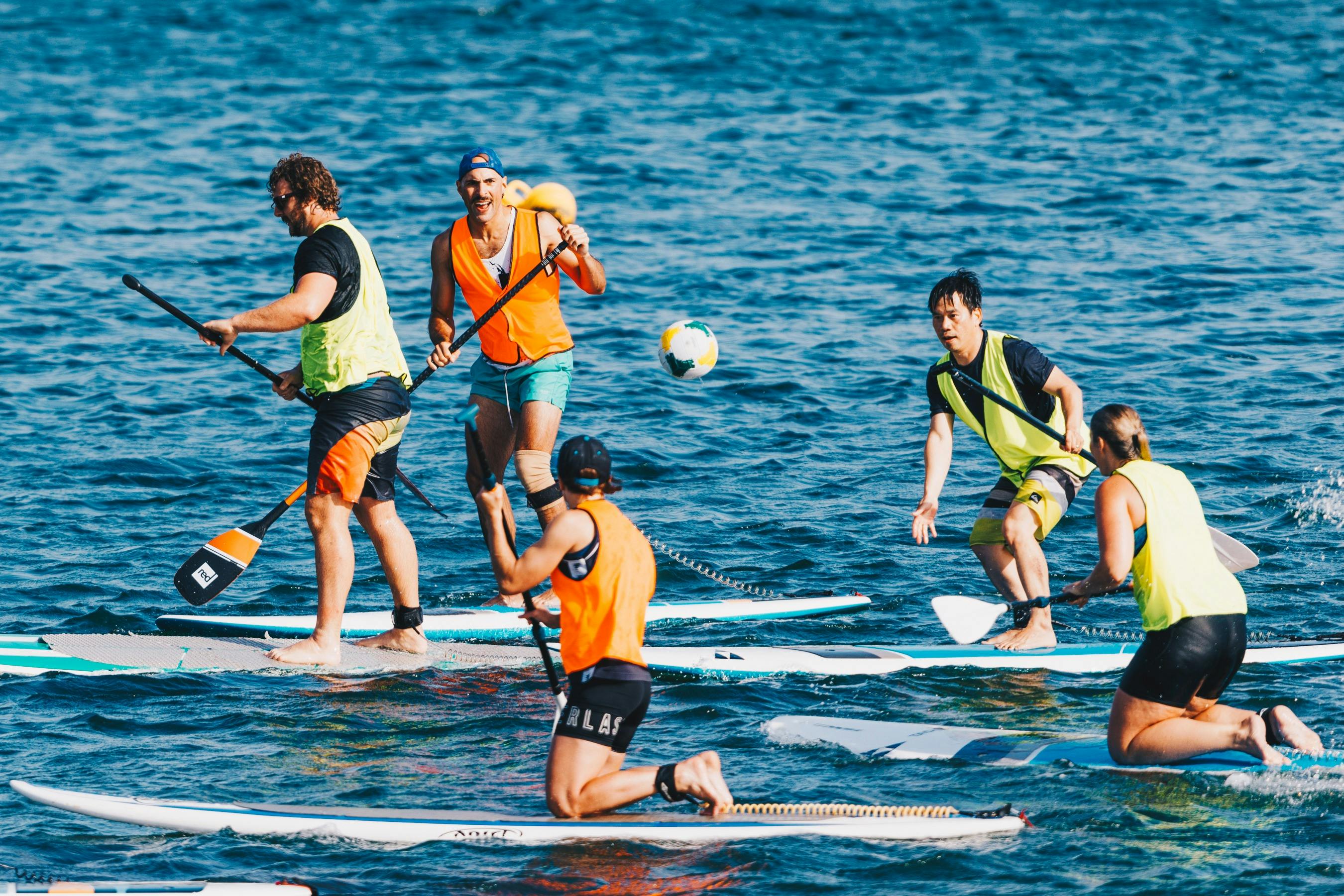 People on stand up paddle boards in high-vis vests, playing a game of SUP ball