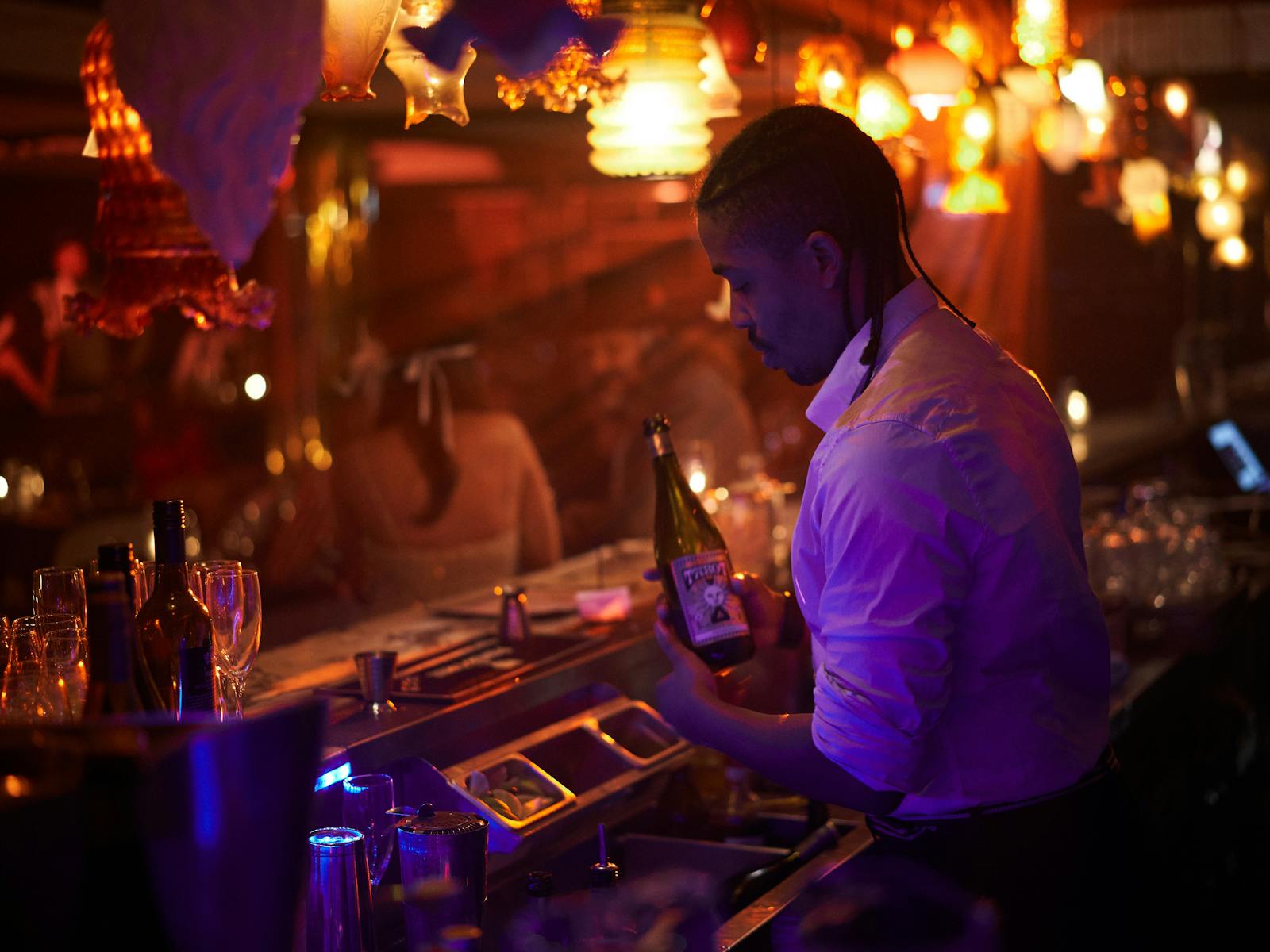Bartender from Potts Point Hotel behind bar making cocktails in the Bamboozle Room. Vintage lamps