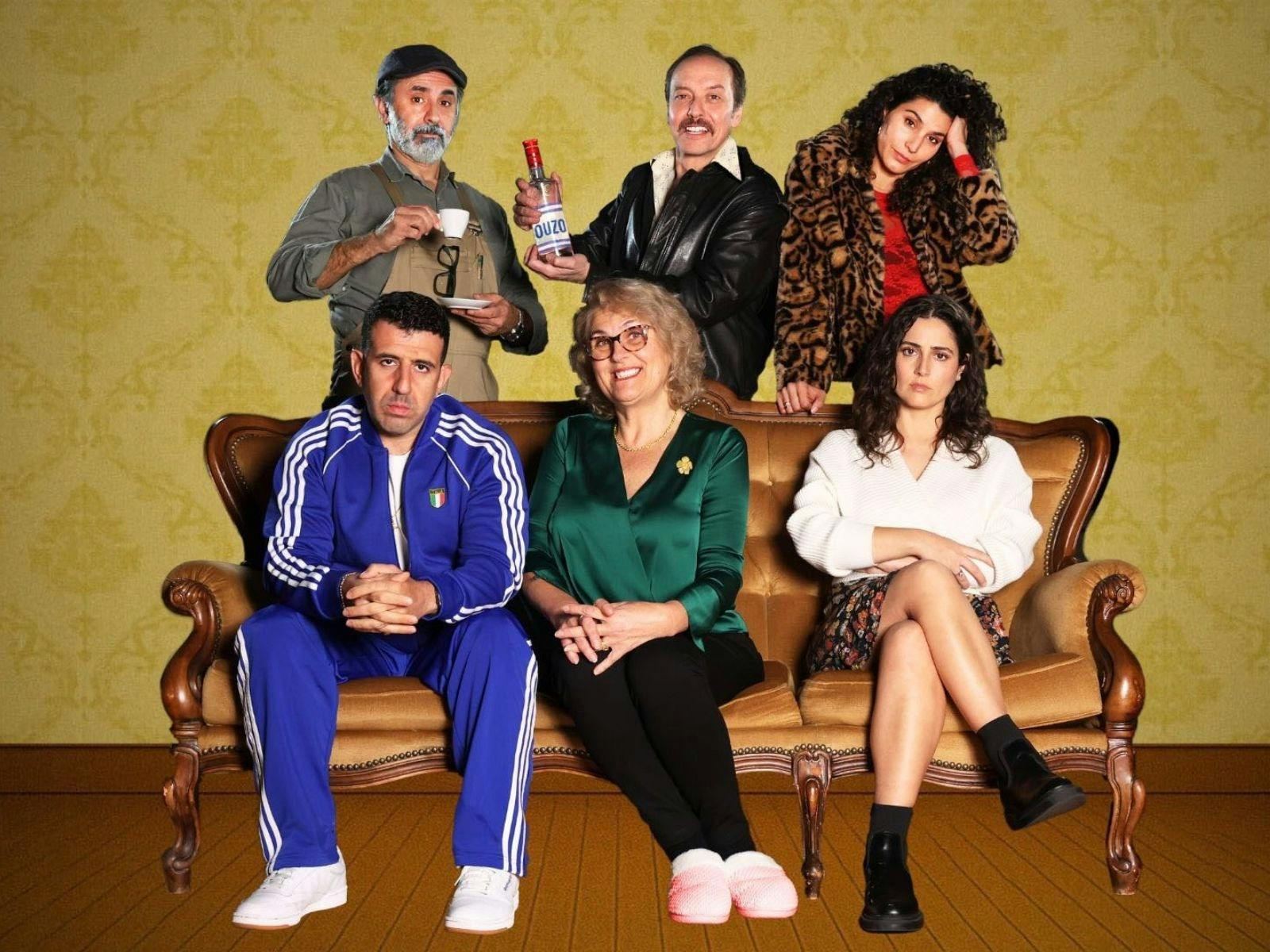 Three people sit on a couch with three people standing behind them, all looking into the camera