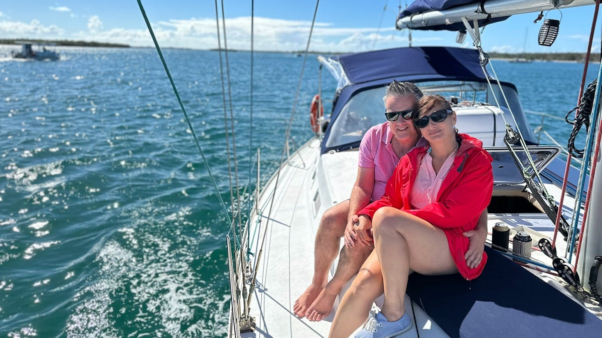 Lady in red and man in pink sitting on the deck of Sun Sailing's yacht during a sunset shared cruise