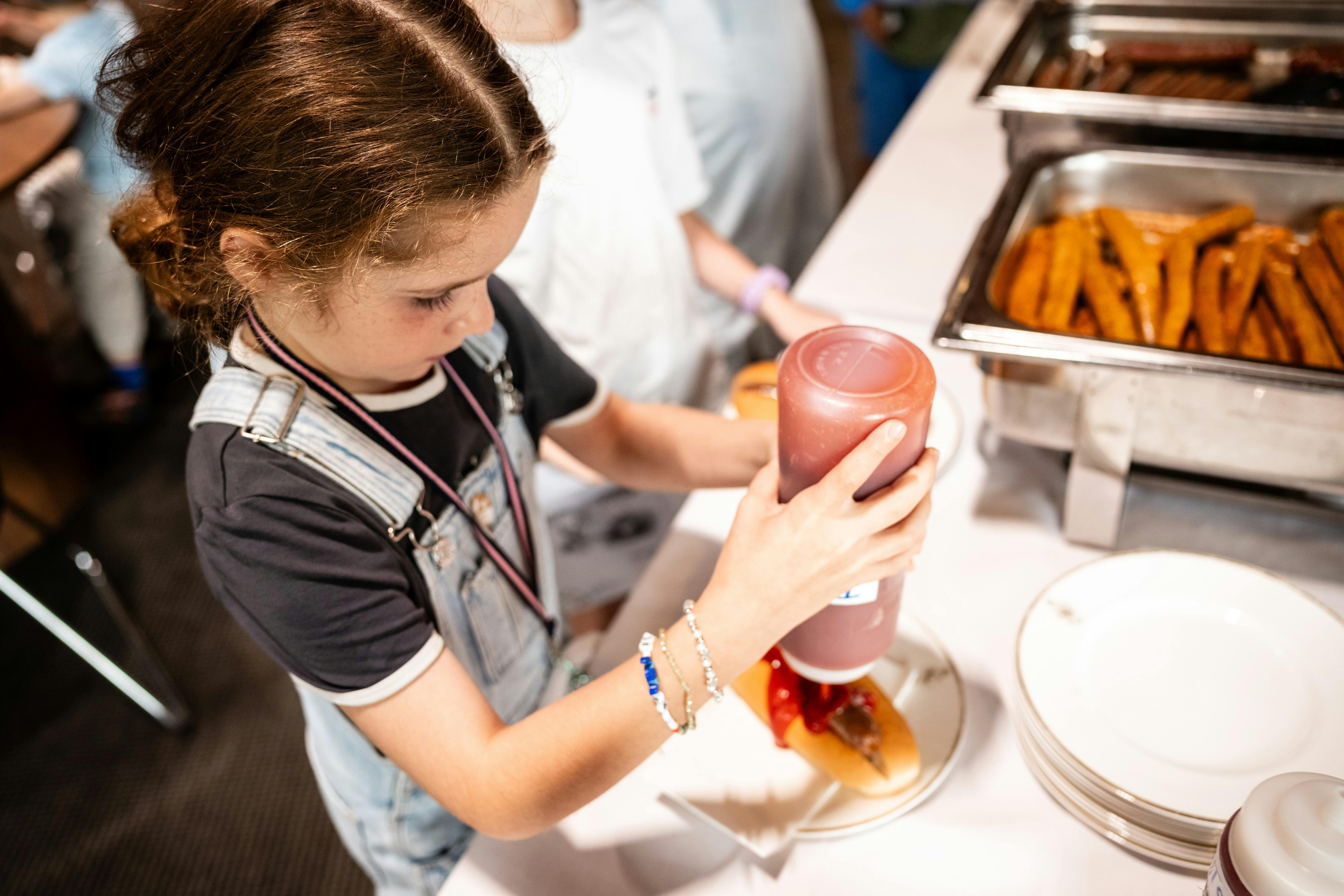 A young girl adds tomato ketchup to a sausage sizzle at amily Fun Day at Parliament of NSW