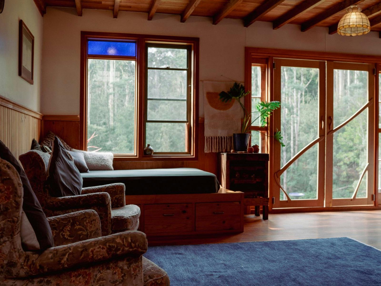 A sun filled cabin with daybed and armchairs overlooking lush forest.