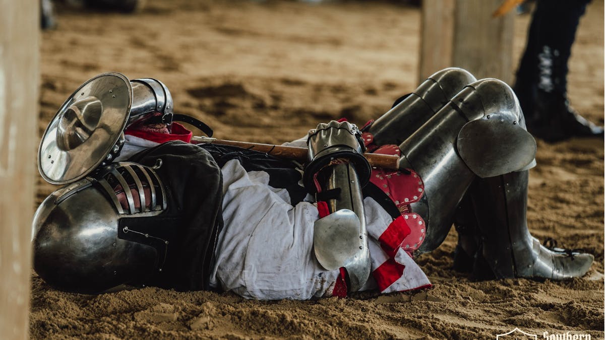 Knocked-down armored knight lying in the sand during a Buhurt combat match.