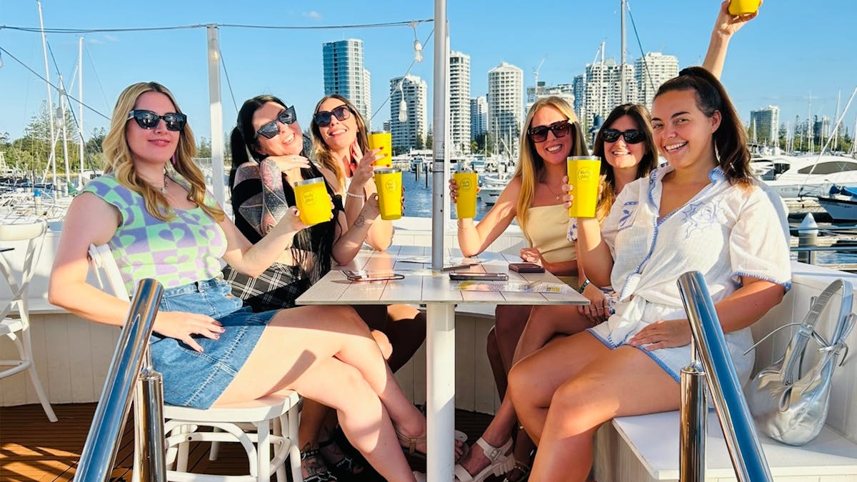 6 women dining at Holy Ship under an umbrella holding up their bright yellow cups
