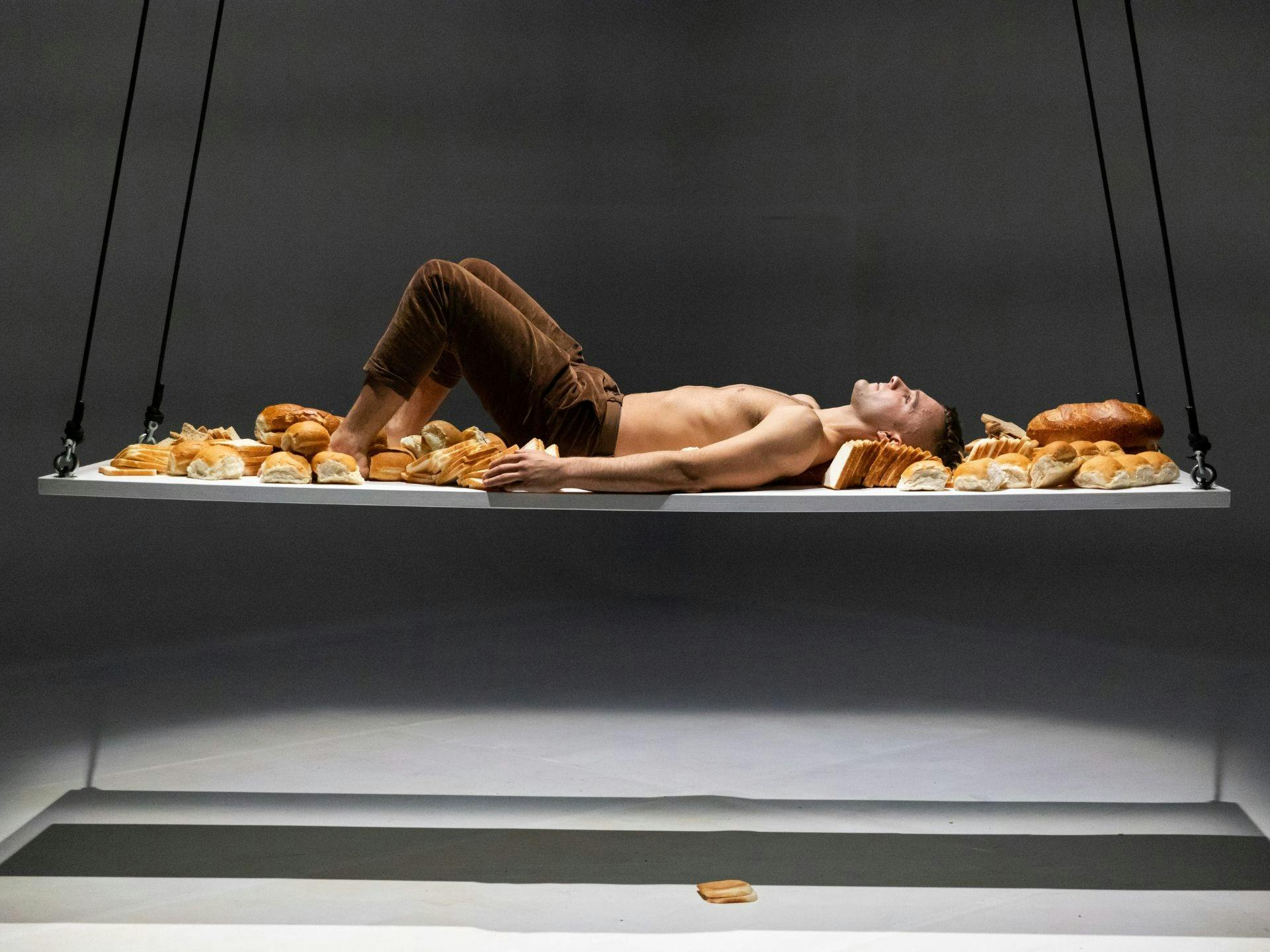 An acrobat lying on a suspended platform filled with bread