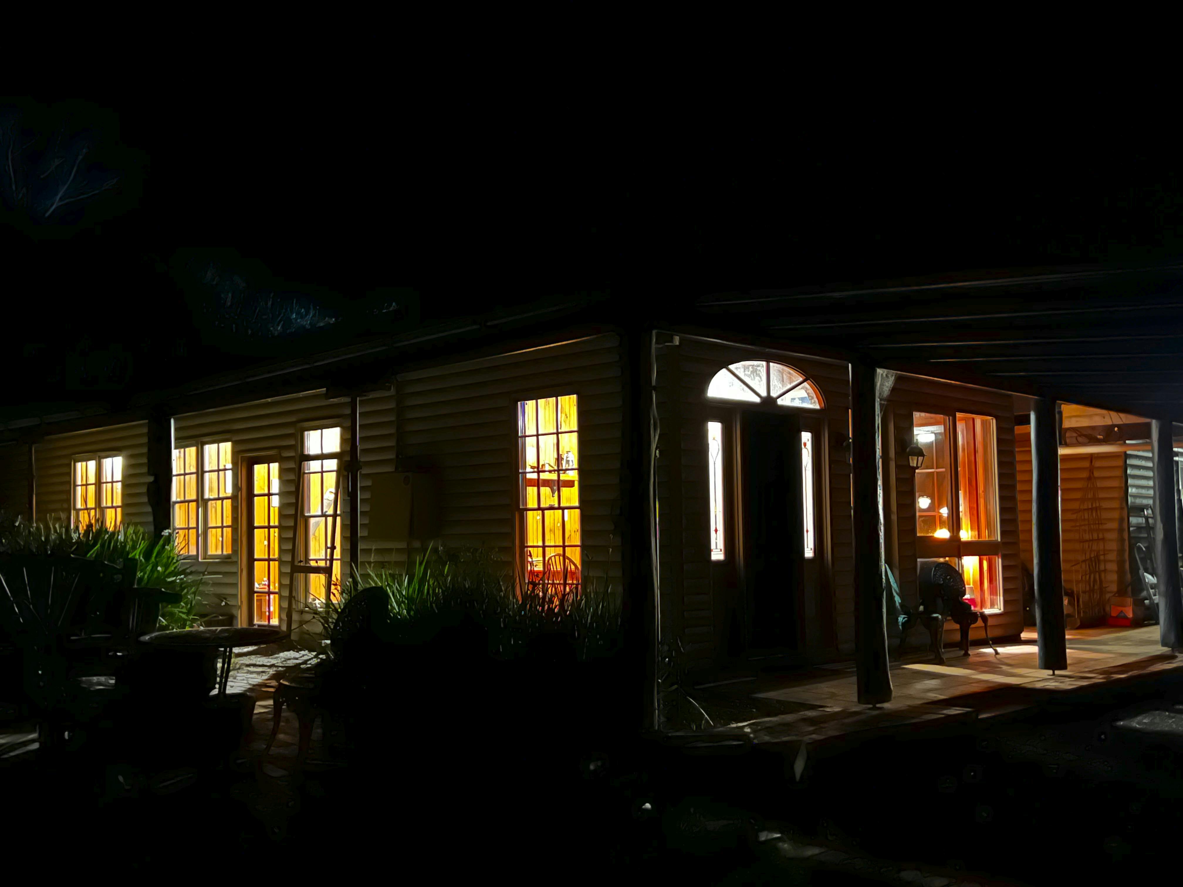 Wollemi Cottage at dusk, with warm light shining through the windows and across the front veranda