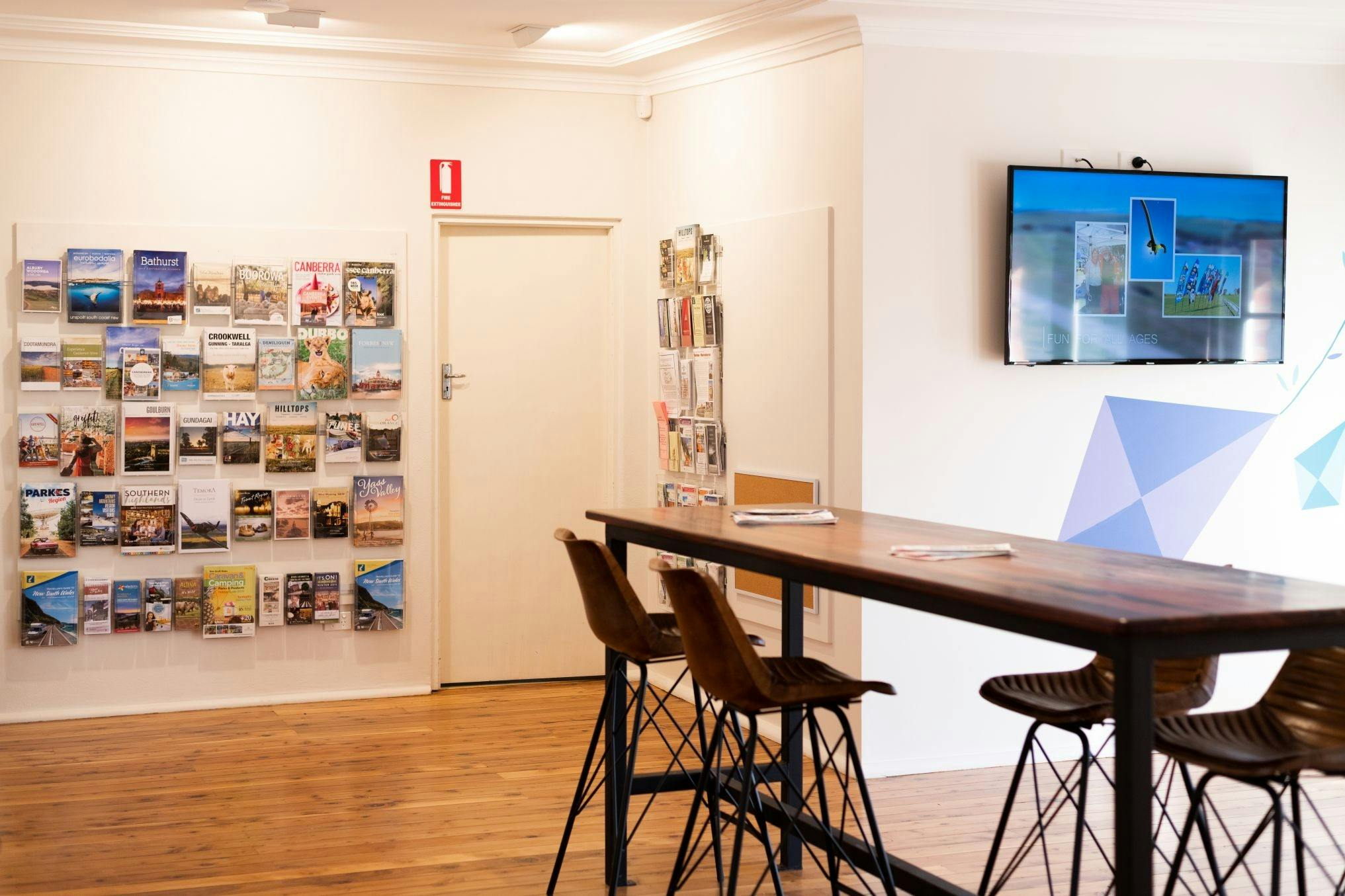 Interior with table, chairs for visitors, a TV with Hilltops videos & a shelf of tourism brochures.