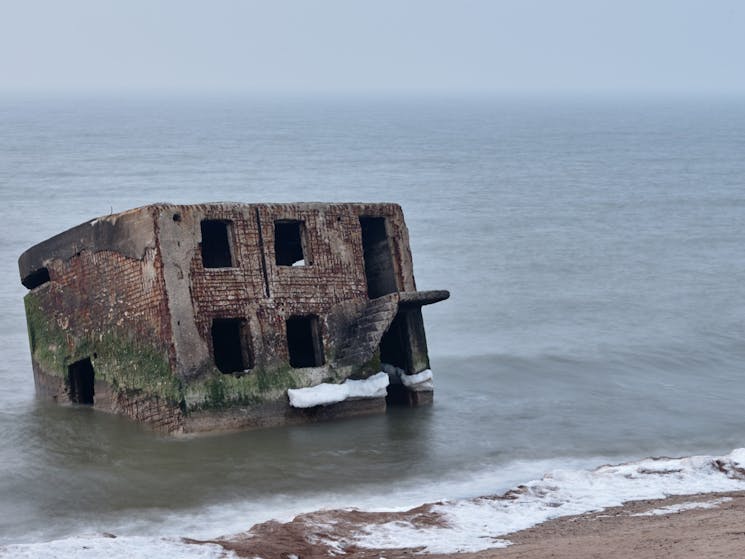 Derelict building in the ocean on foggy day by the shore with rolling waves.