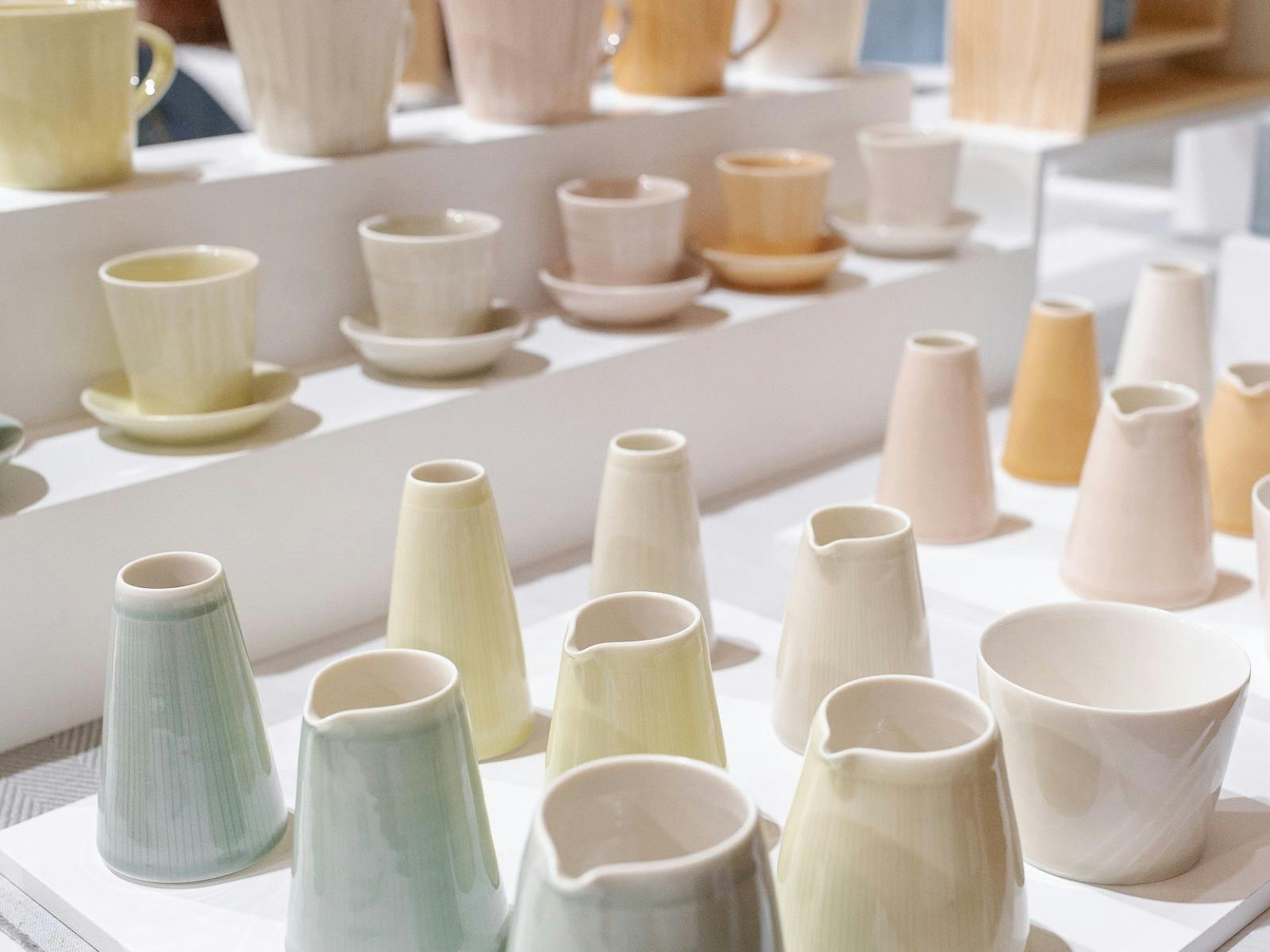 Handmade ceramics in a variety of pastel tones on a white tiered market stall layout.