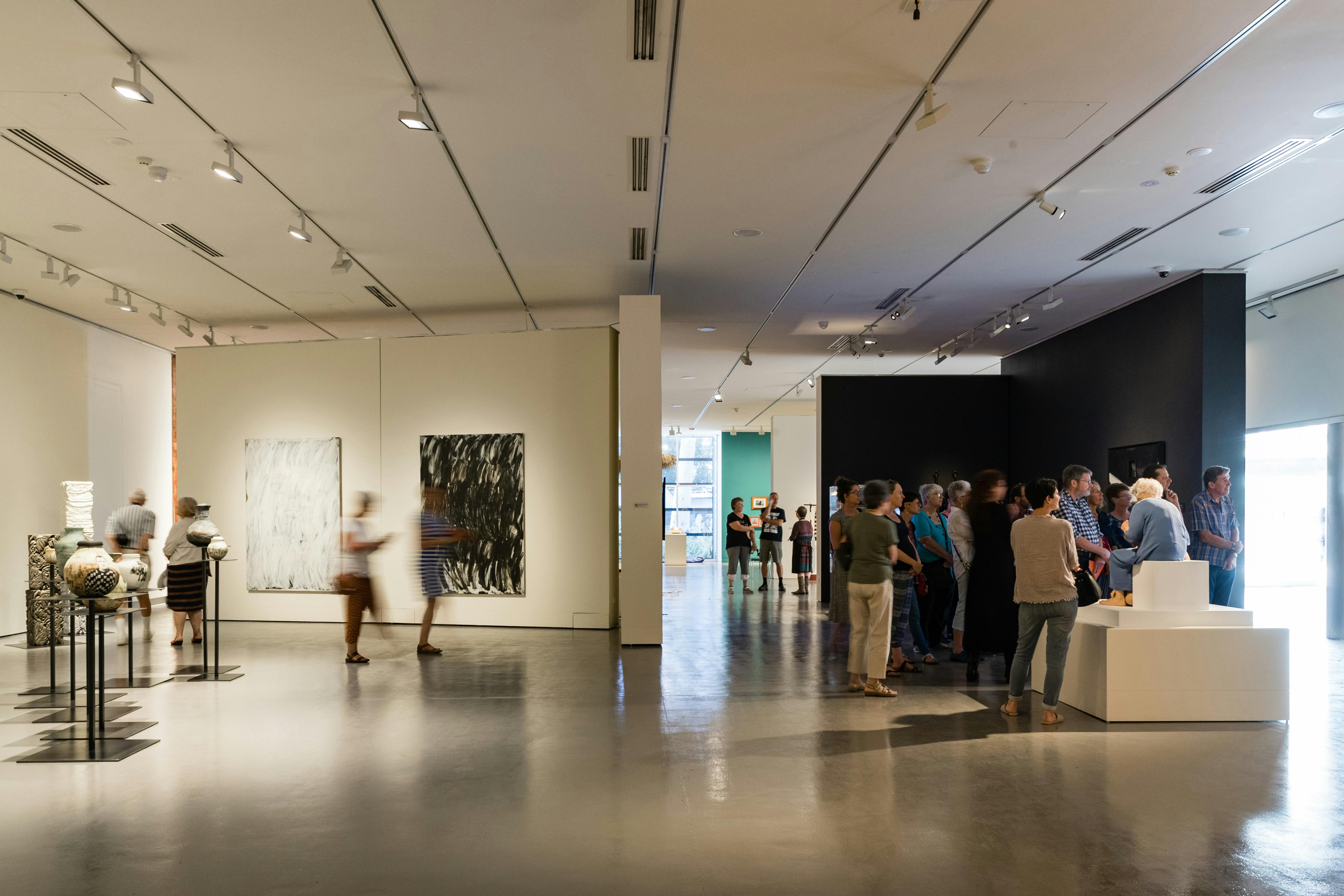 people walking through art museum enjoying works on wall and sculptures.