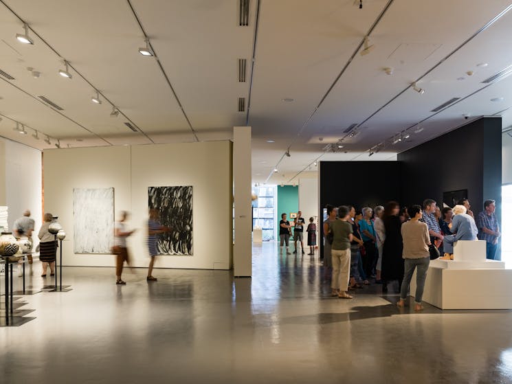 people walking through art museum enjoying works on wall and sculptures.