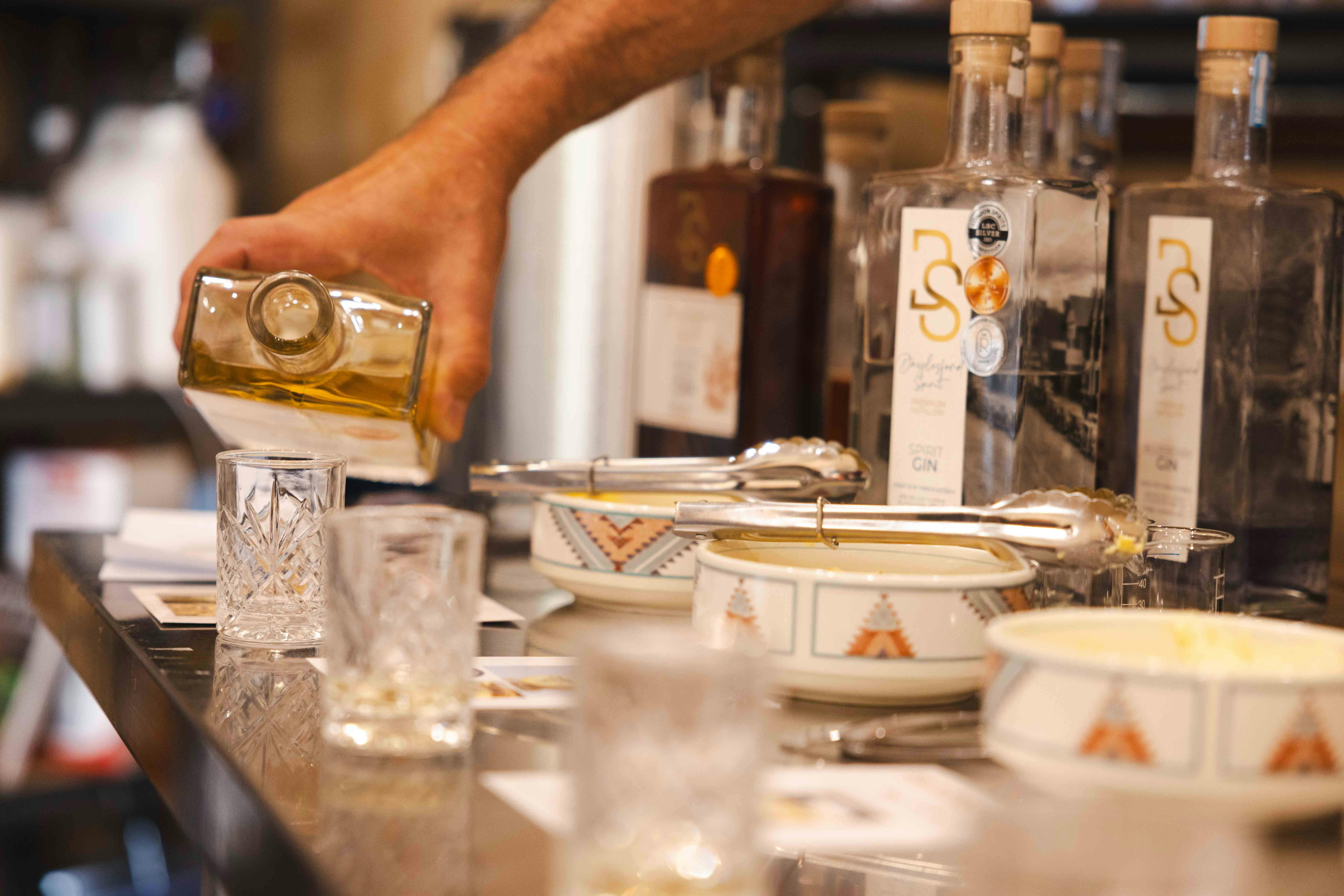glasses in foreground.  Hand pouring gin into glasses