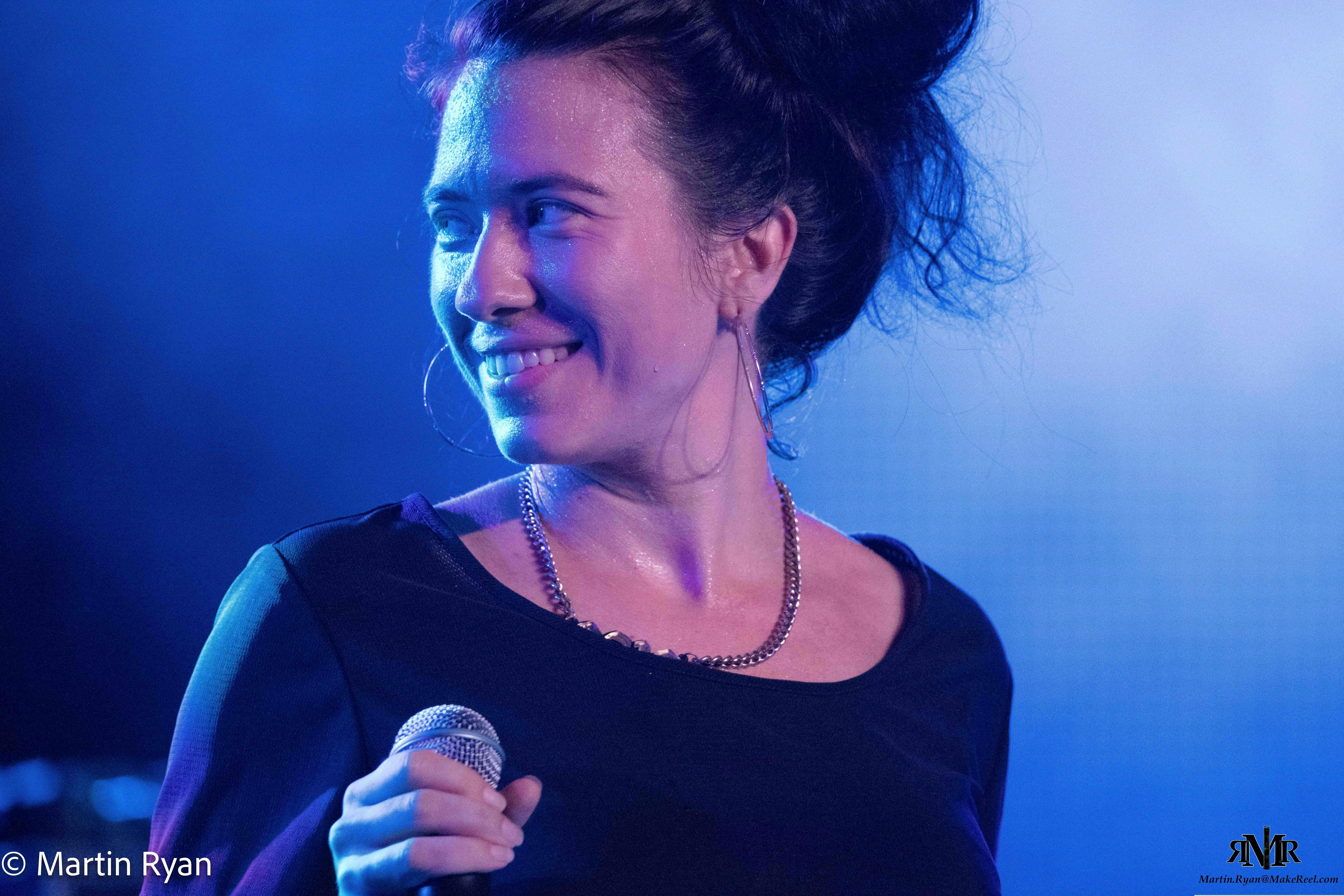 A woman with dark hair in messy bun  is smiling at an audience with head turned