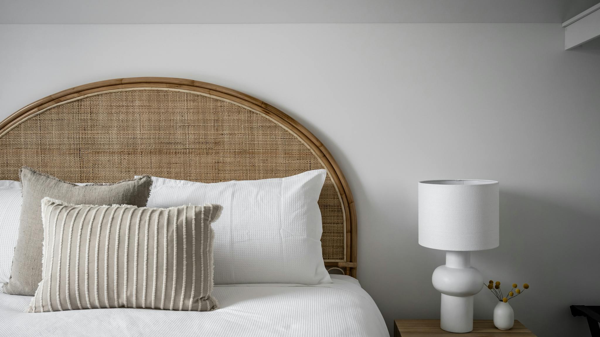 King size bed with rattan bed head and white linen, with decorative white lamp.