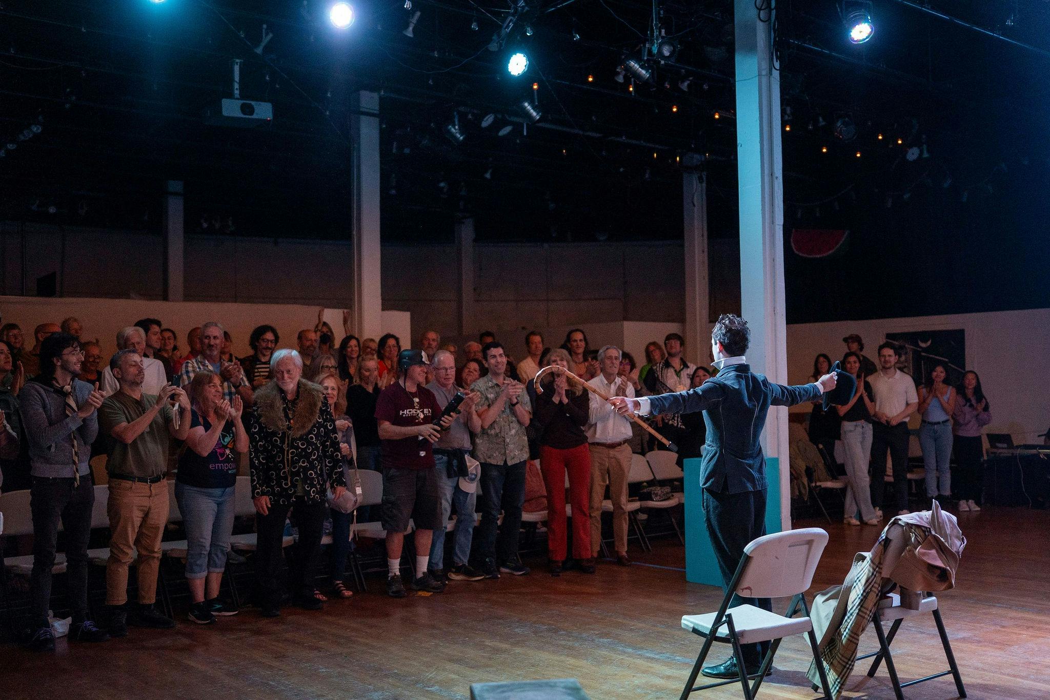 A man stands on stage with his arms outstreched while the audience gives a standing ovation