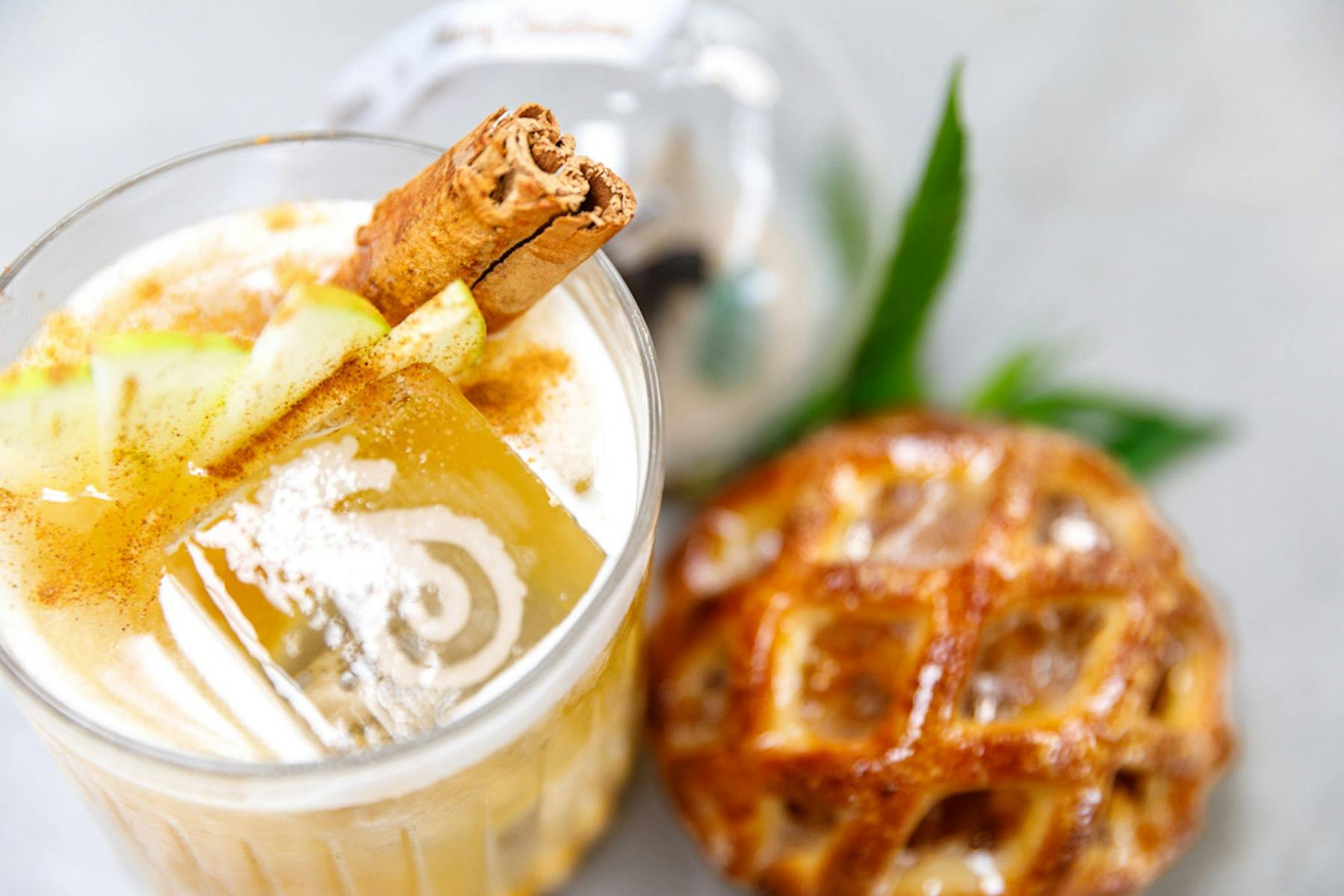 A picture of an apple based cocktail, garnished with cinnamon  and apple, beside an apple turnover