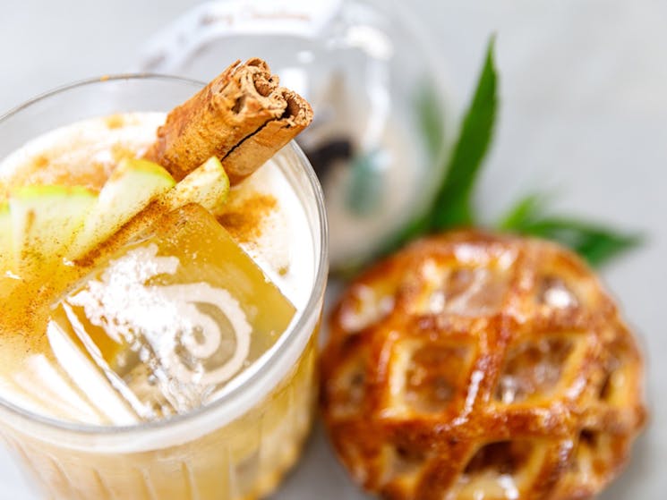 A picture of an apple based cocktail, garnished with cinnamon  and apple, beside an apple turnover