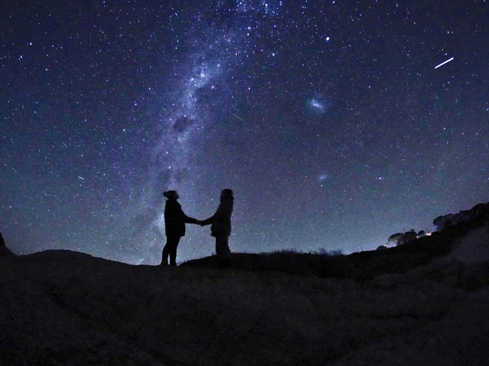 Two people in silhouette beneath a star‑filled sky and the Milky Way.