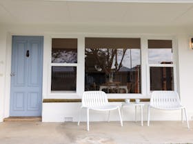 Front veranda with two outdoor chairs, a small table and the blue front door of the home.
