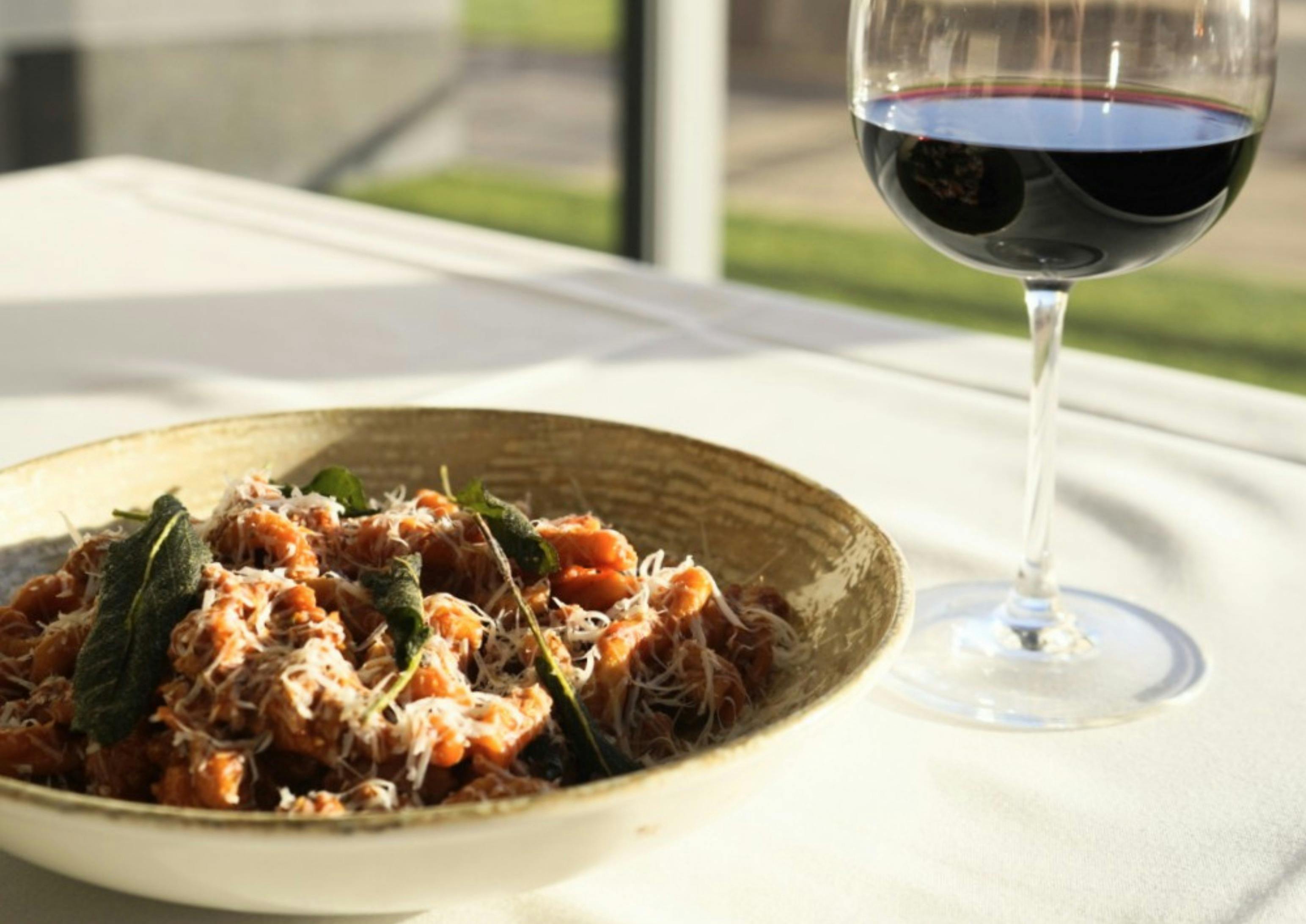 A glass of red wine with a bowl of pasta