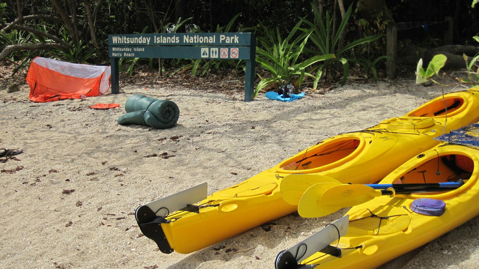 Two kayaks on beach with sign and tent in background.