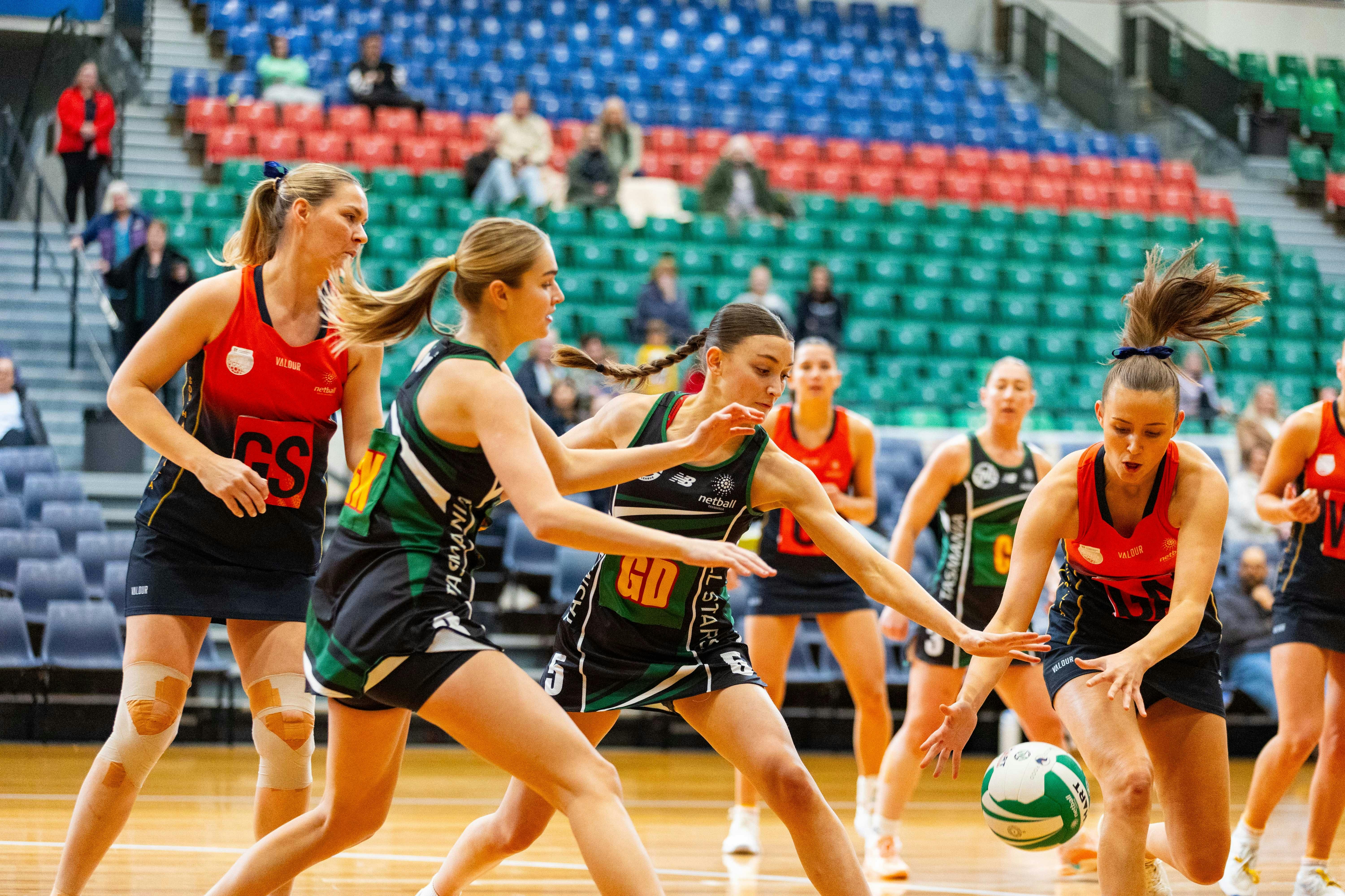 Two players leaning down to grab a netball