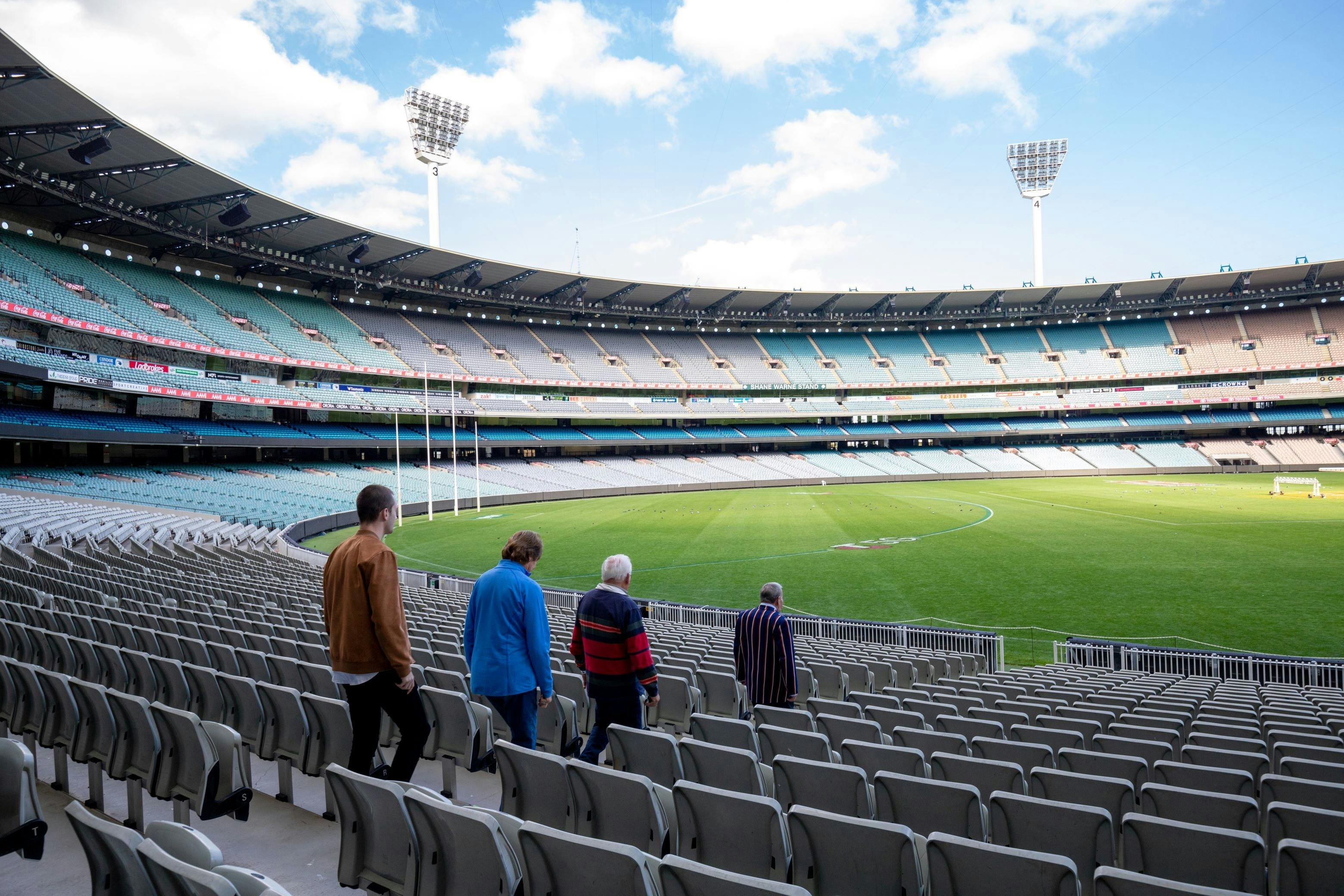 Four men walking through the stands to the ground of the MCG