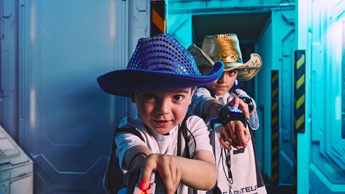 Two young boys in cowboy hats point their wrist devices at the camera in game gear.