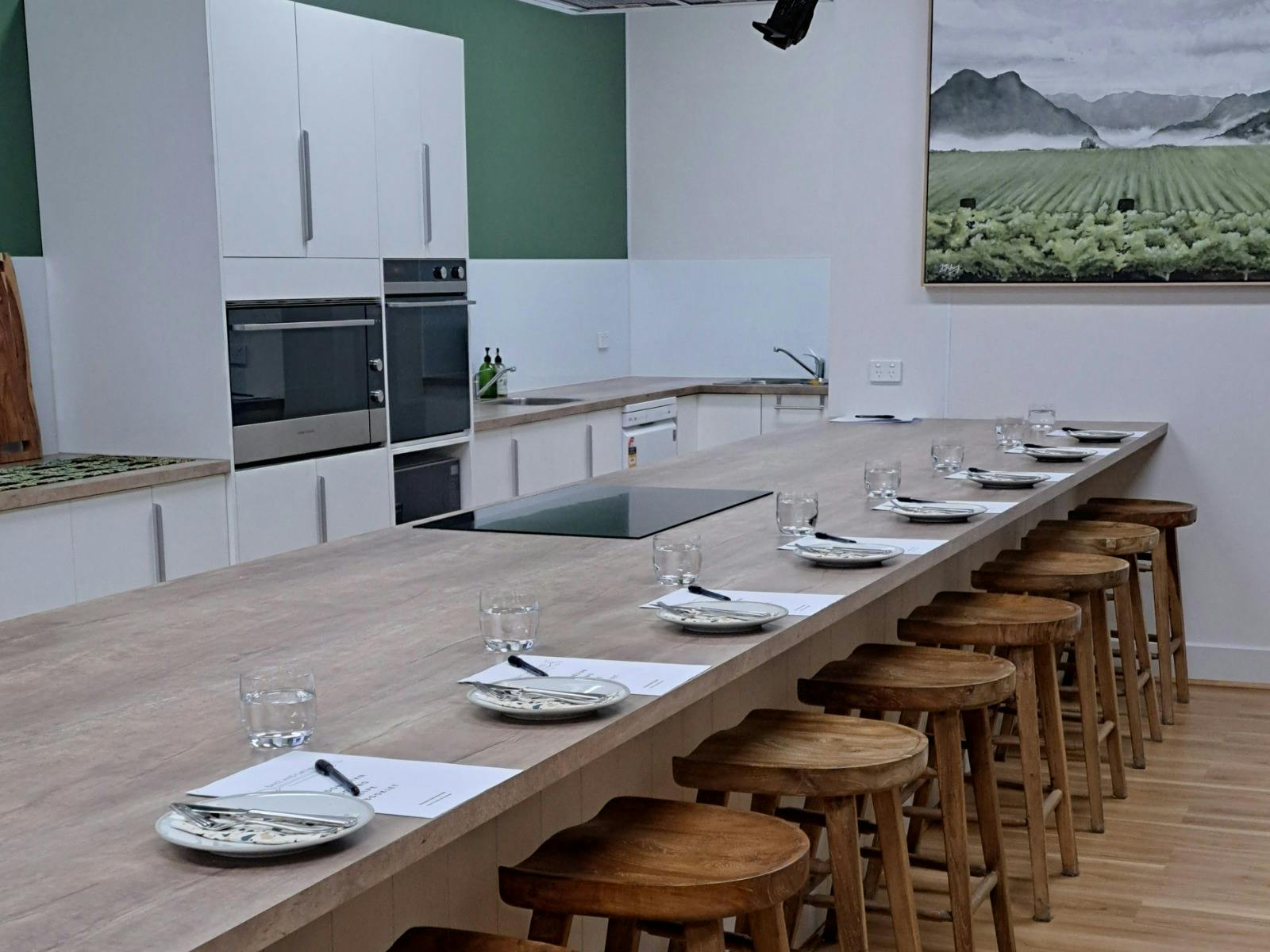 Bake and Gather kitchen ready for class with recipe booklets, cutlery, stools under 6 metre bench.