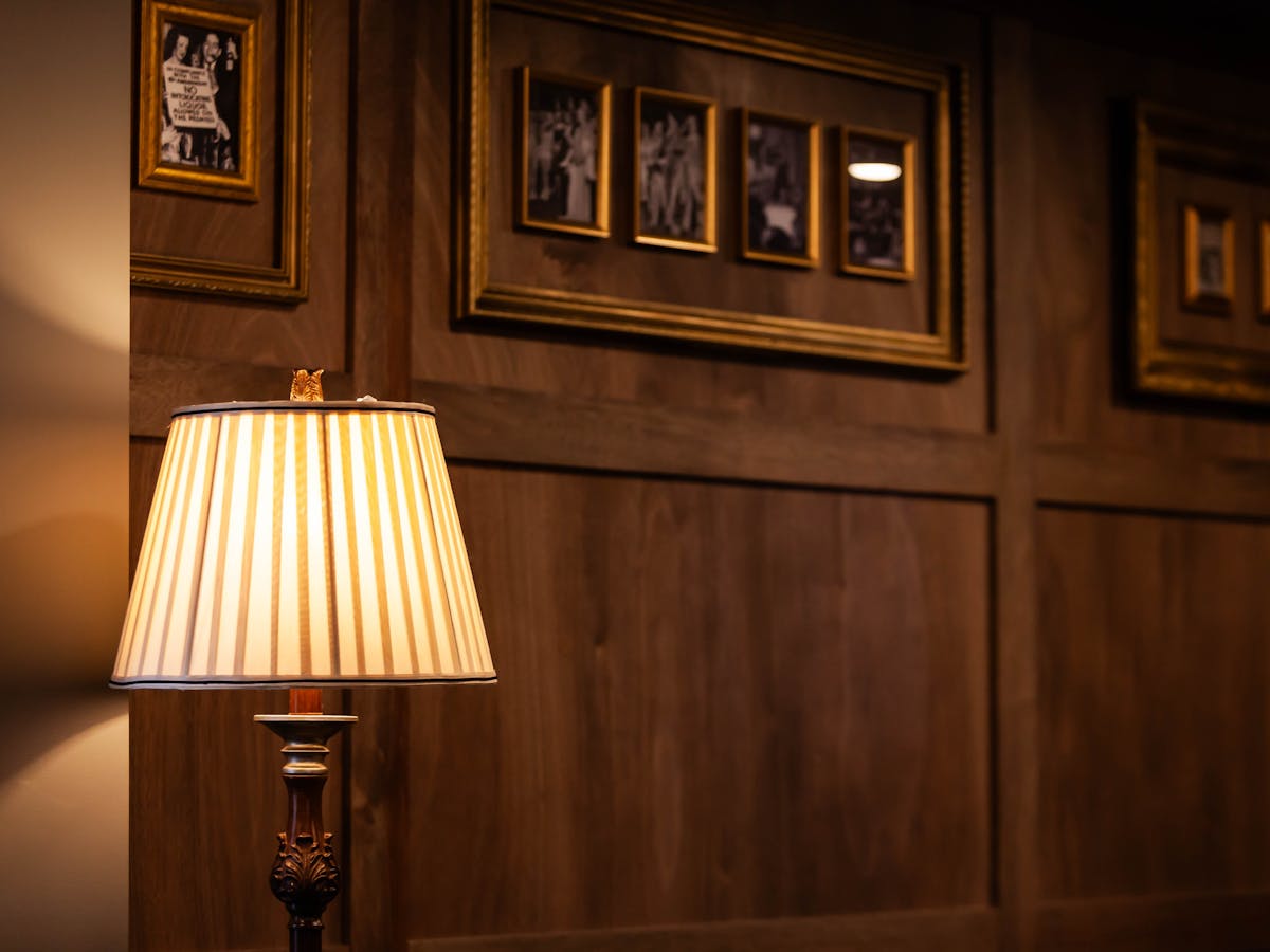 A lamp in front of a wooden panelled wall with historical photographs and art