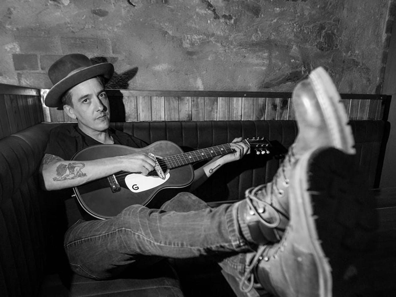 Ap D'Antonio sitting on a couch playing guitar