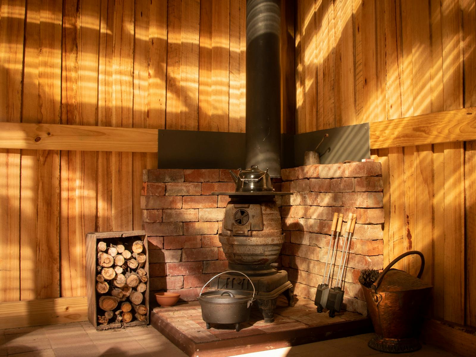 A small wood fired stove sits in the corner of a rustic shed, surrounded by red bricks.