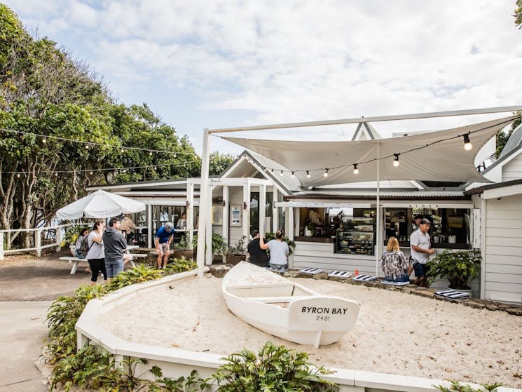 Outside of the Beach Kisok cafe, boat in sand pit and people sitting around.