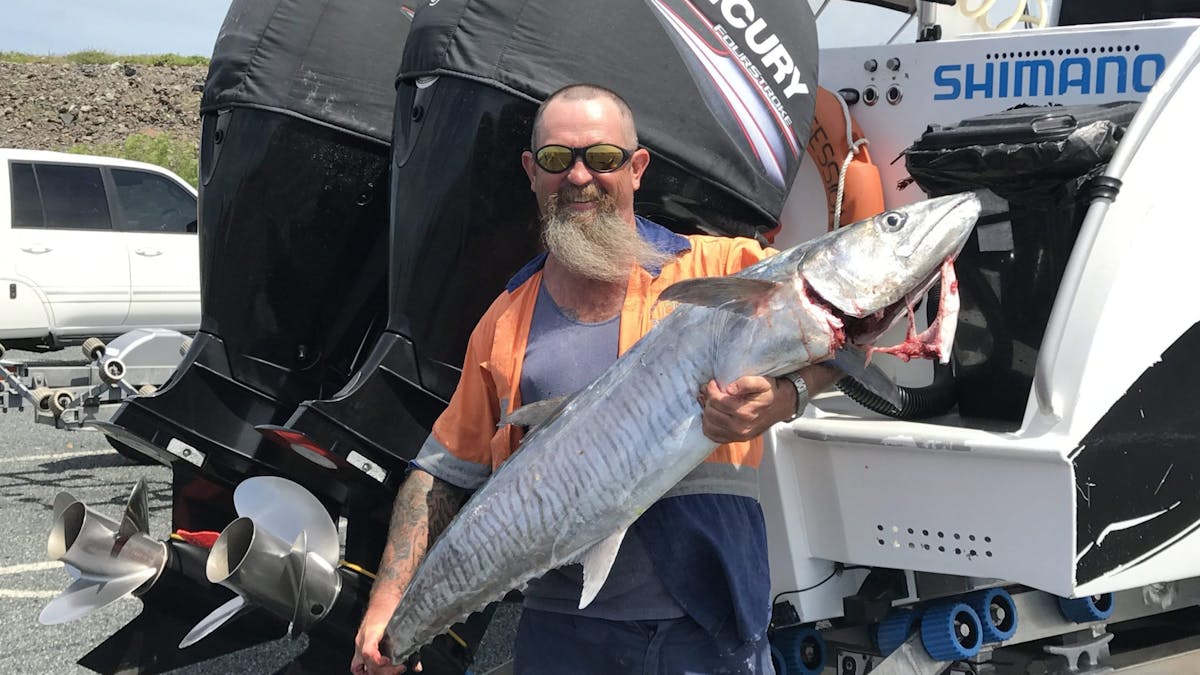 Angler hold up a large Spanish Mackerel standing behind the boat. The 2 large motors are behind him. Angler hold up a large Spanish Mackerel standing behind the boat. The 2 large motors are behind him.