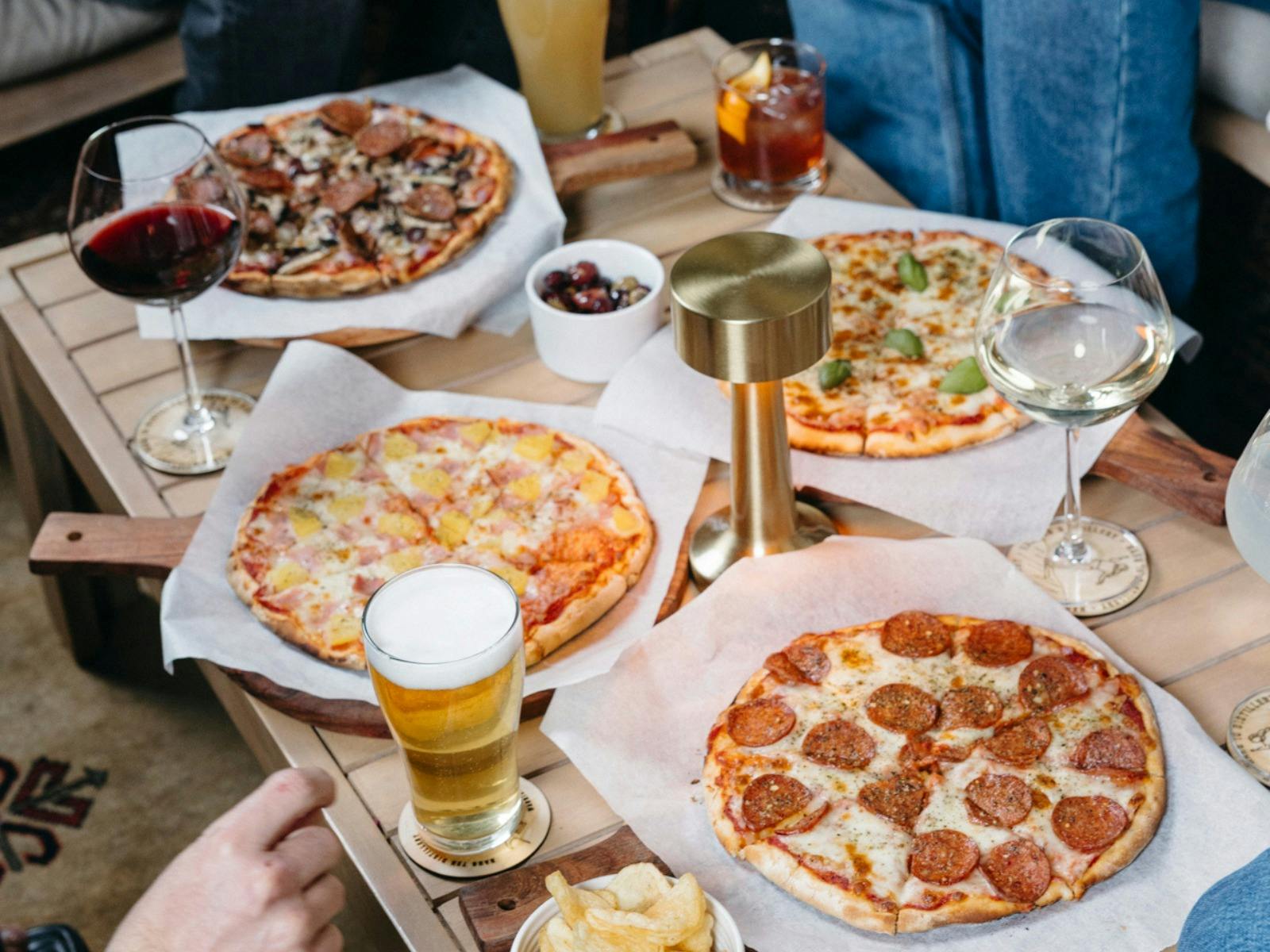 Four types of pizzas with beer, wine and cocktails on a table