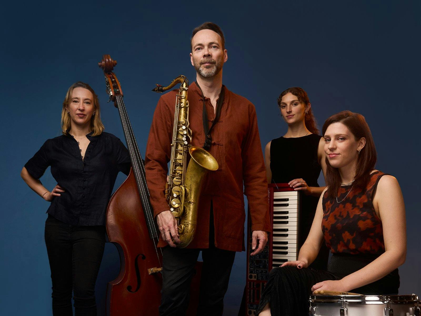 Male holding saxophone standing with three female musicians holding instruments.
