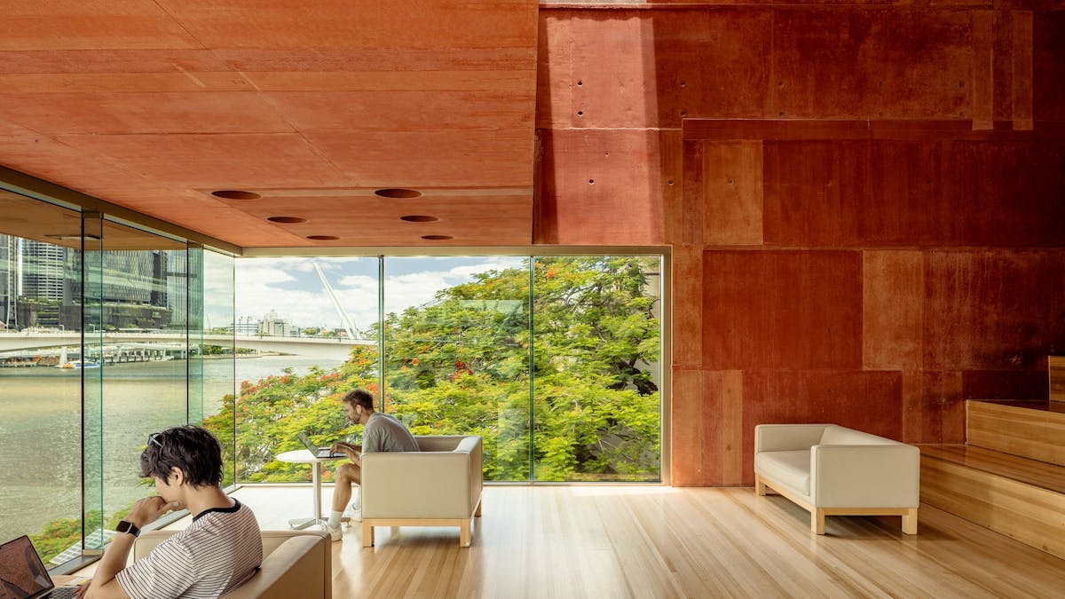 people engaging in quiet independent study in a red room, with glass walls and river backdrop
