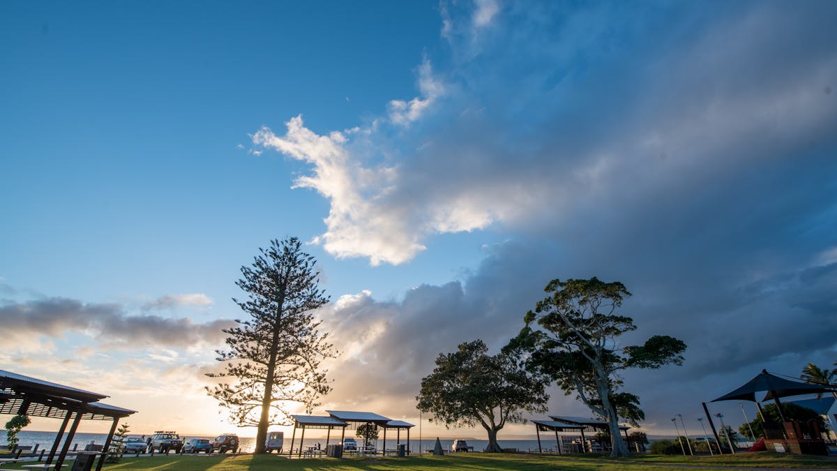 Sun peeking through clouds over BBQ and grassy play areas at Cleveland Point Recreation Park, QLD.