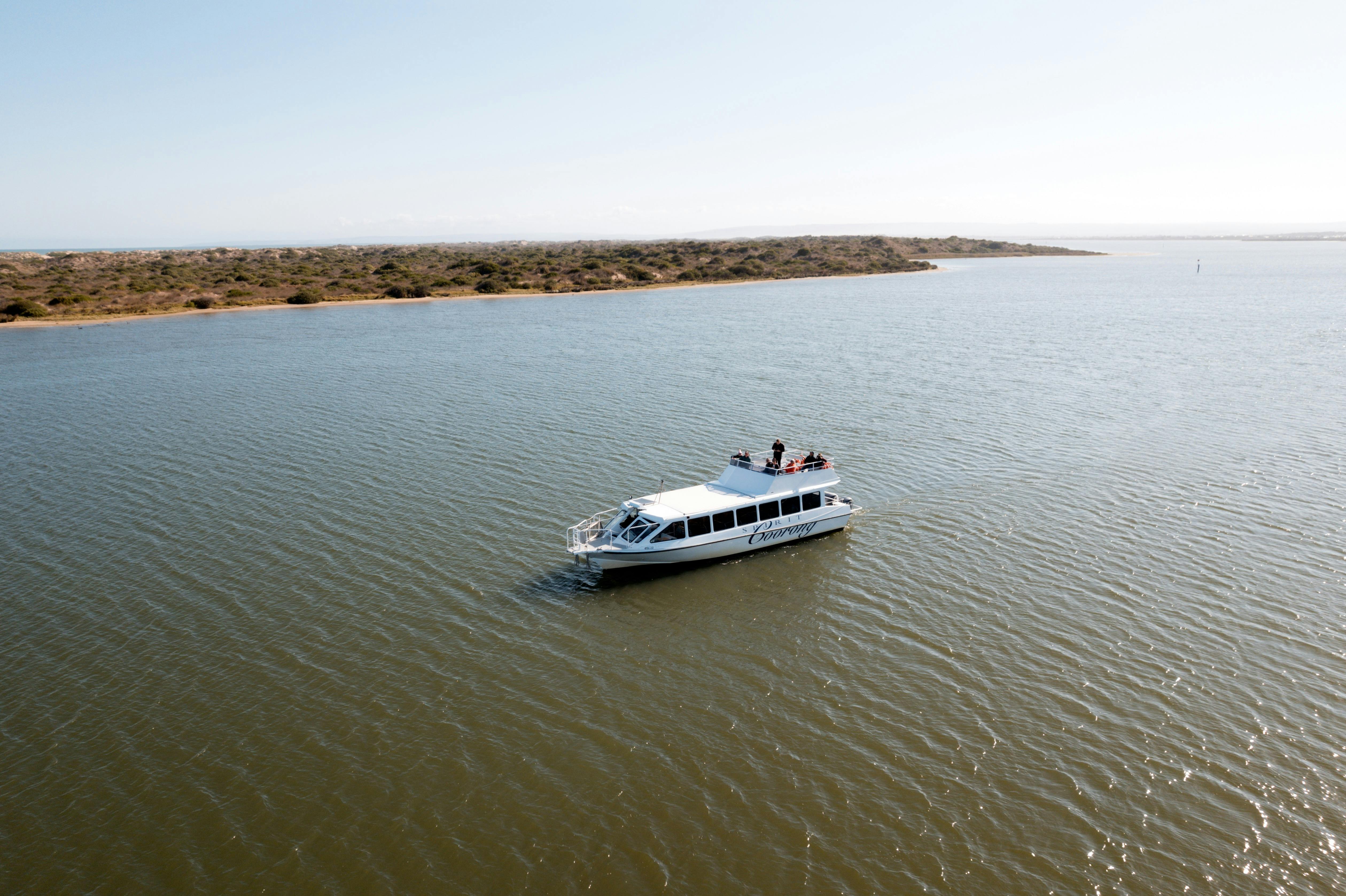 The "Spirit of the Coorong" boat cruises on calm water, with a scenic shoreline in the background.
