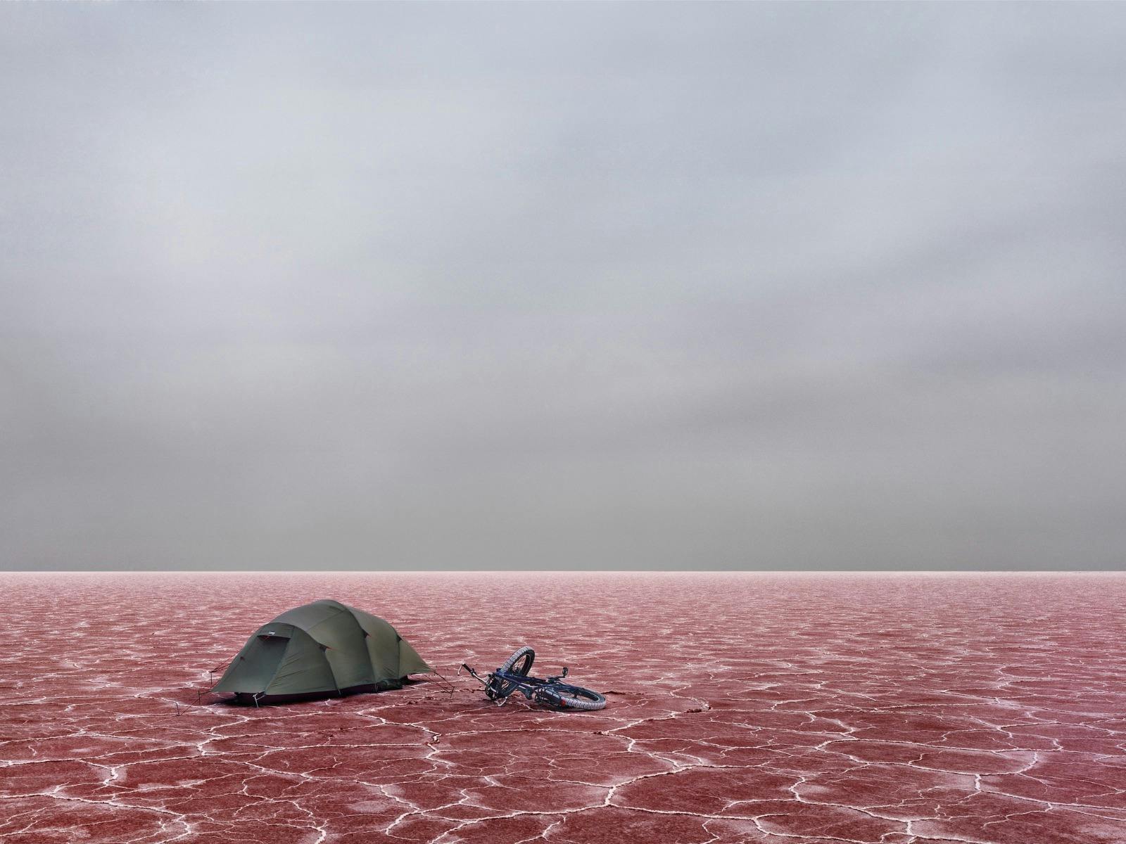 Tent and bicycle on the pink salt flats of Kati Thanda–Lake Eyre beneath a stormy sky.