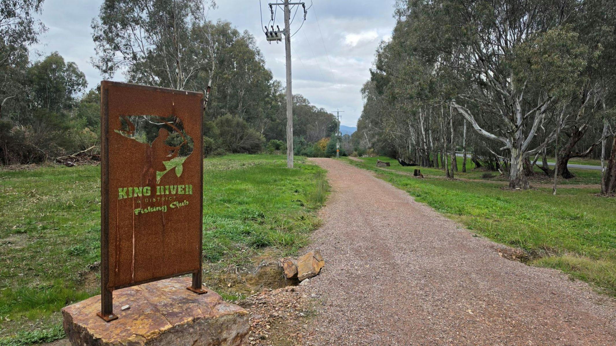 A rustic sign that says 'King River Fishing Club' next to a gravel trail
