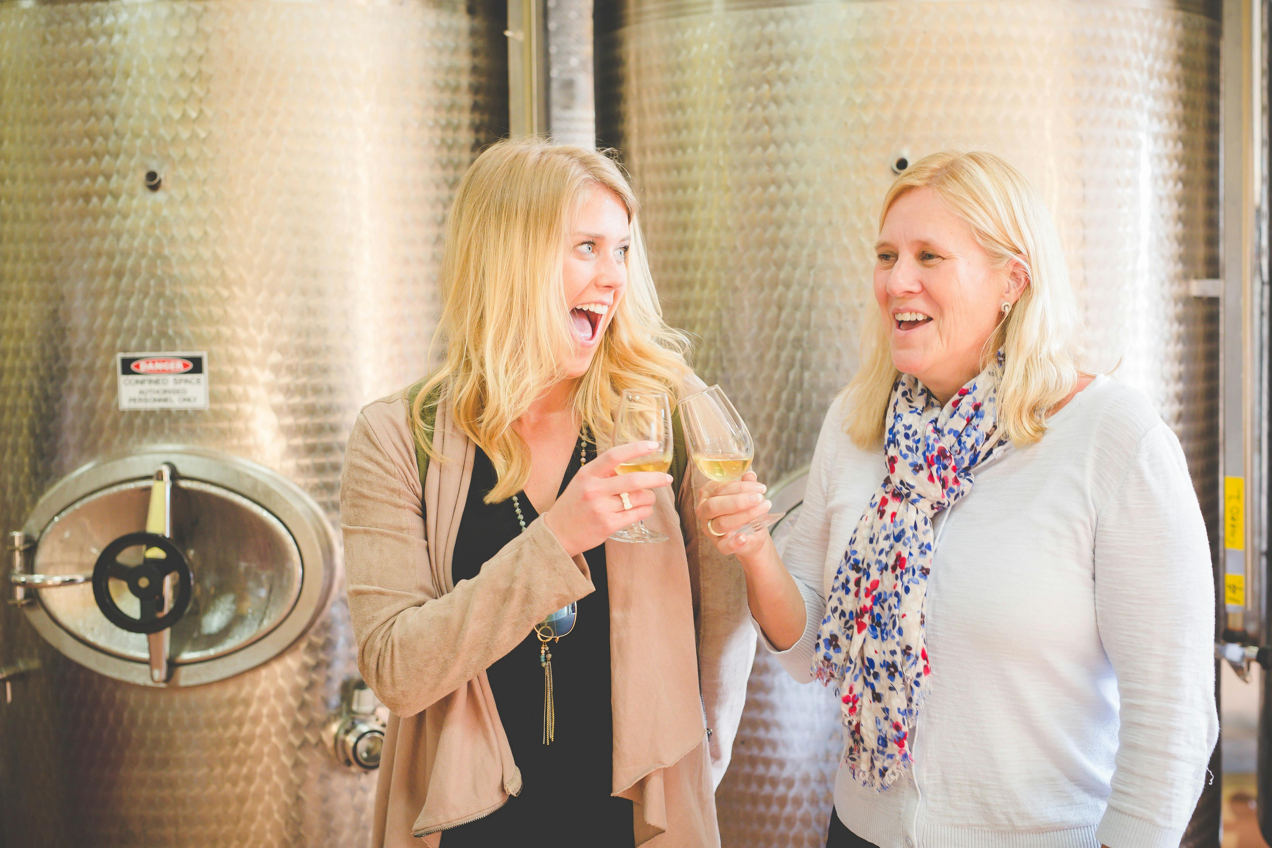 Zwei lachende Frauen halten Weingläser in einem modernen Weinverkostungsraum