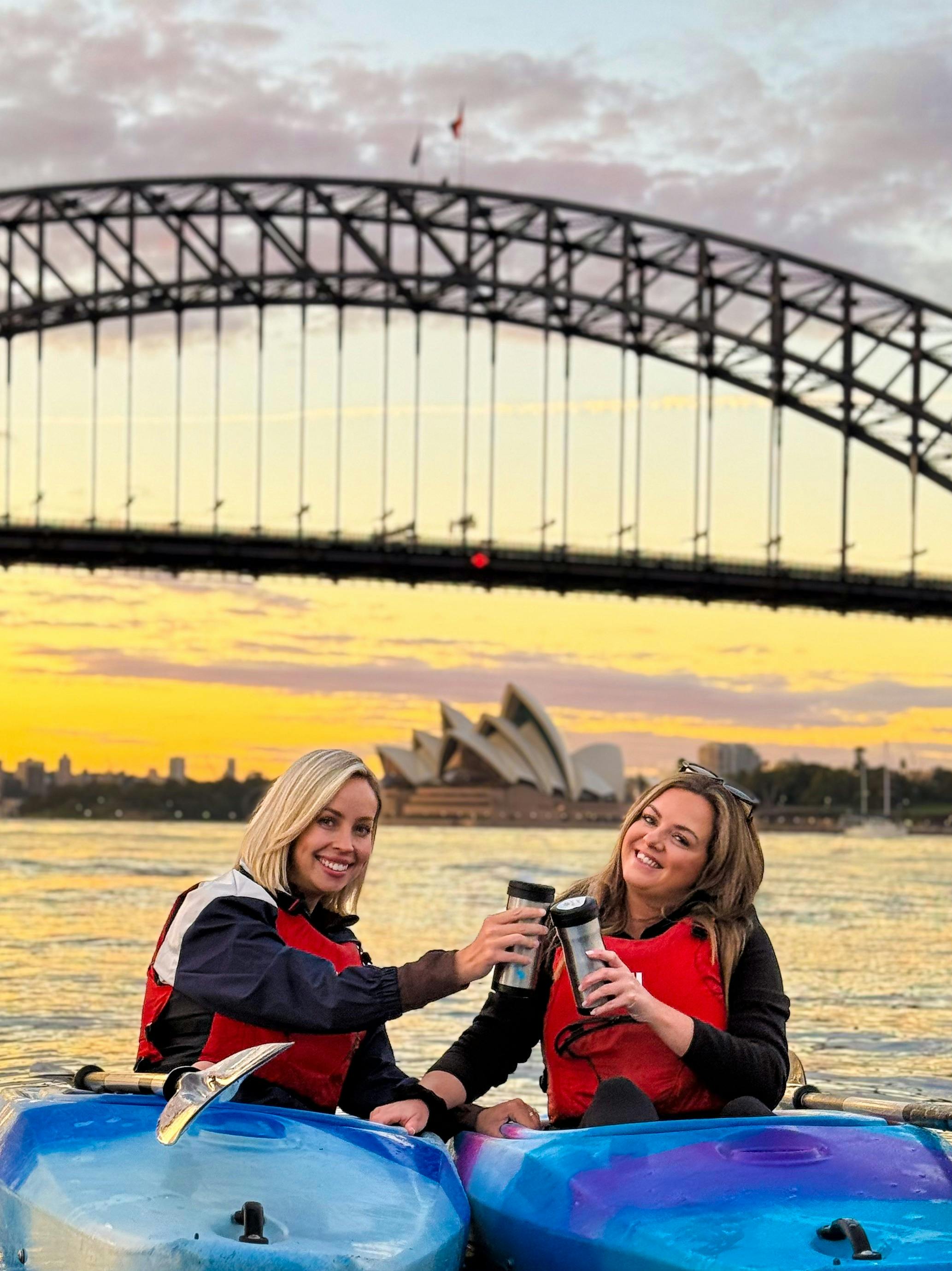 友人たちはシドニー・バイ・カヤックの青いカヤックに乗って、シドニー湾でコーヒーを楽しんでいます。