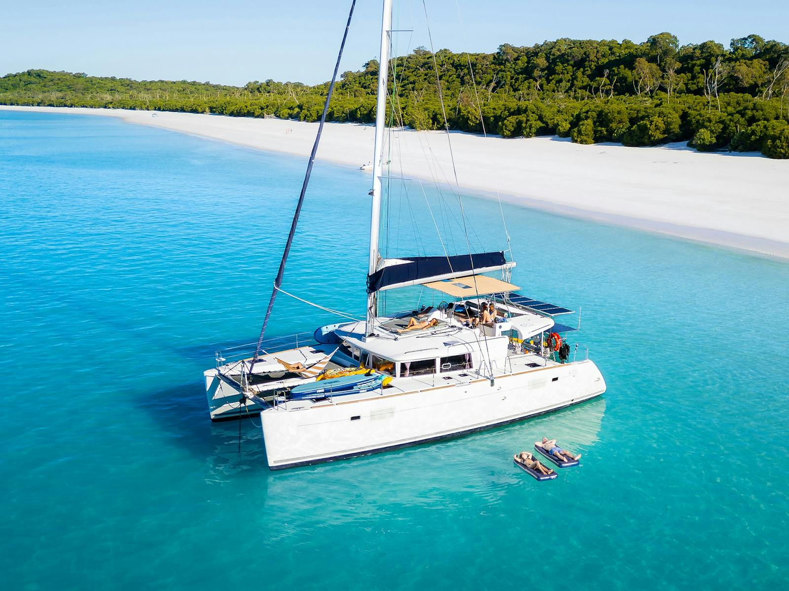 Aerial view of a luxury catamaran in turquoise water beside a tropical white sand beach Aerial view of a luxury catamaran in turquoise water beside a tropical white sand beach