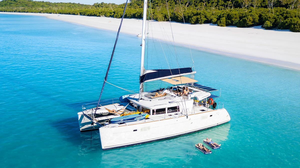 Aerial view of a luxury catamaran in turquoise water beside a tropical white sand beach