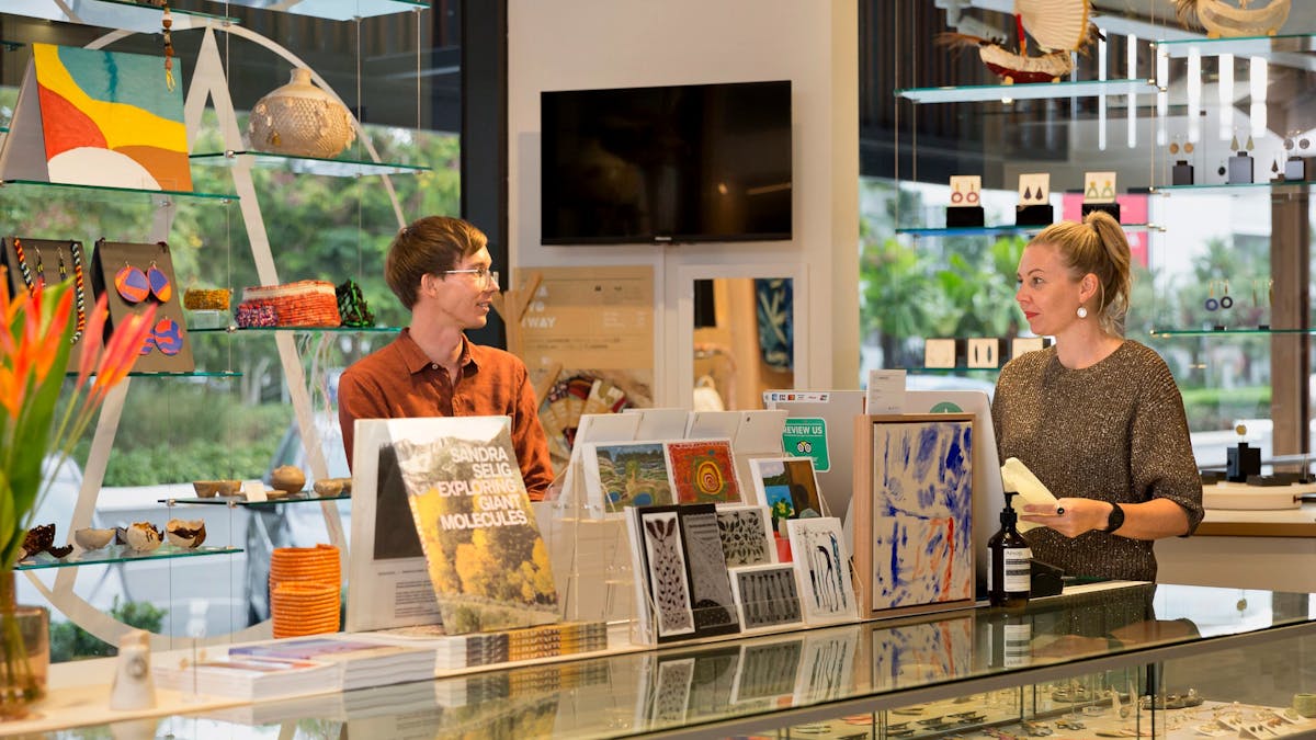 A young man and women chat at the NorthSite Store front desk, near beautiful art, cards & jewellery